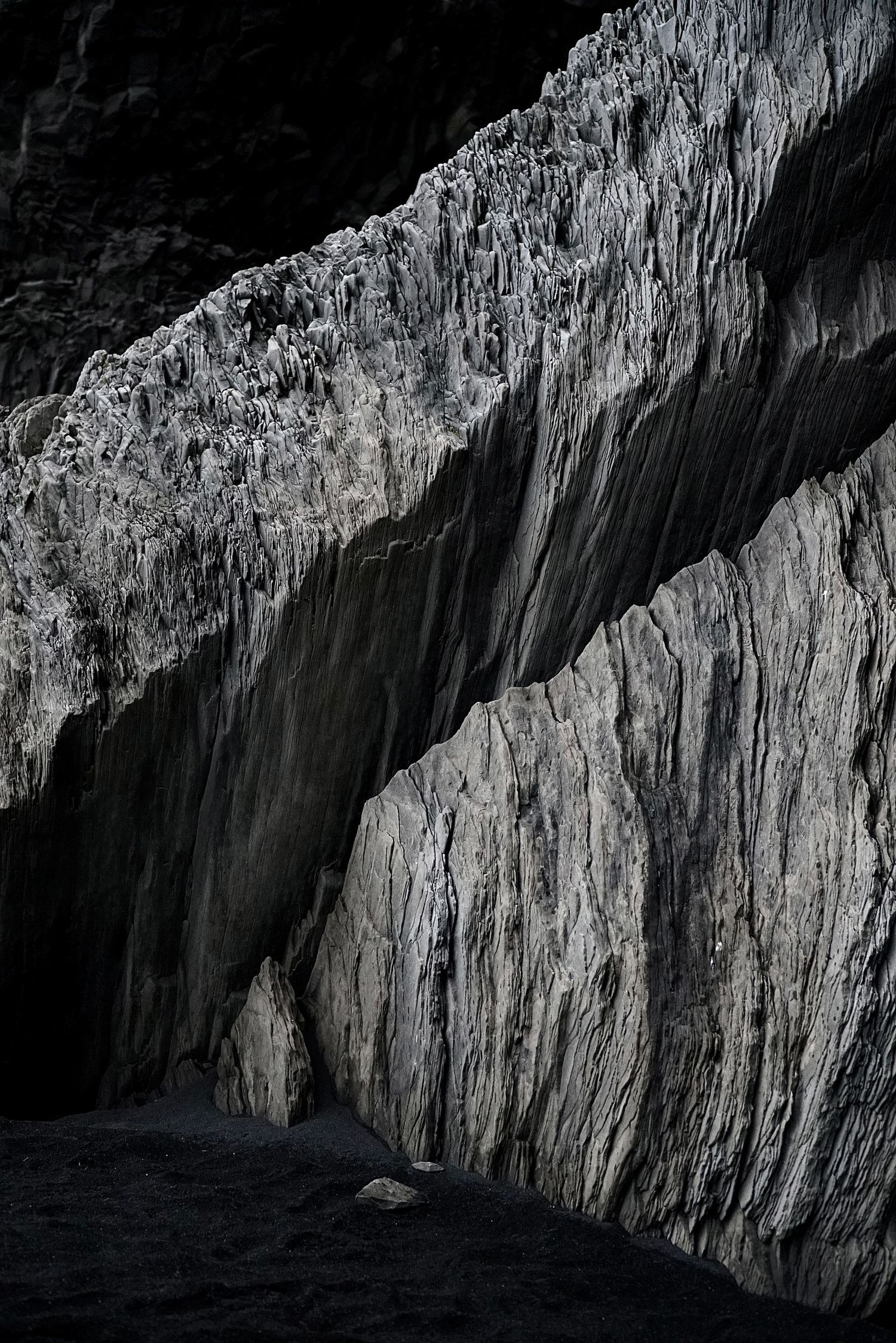 Dark dramatic rock face with jagged textured cliff formations in black and white tones. Black sand beach in Iceland.