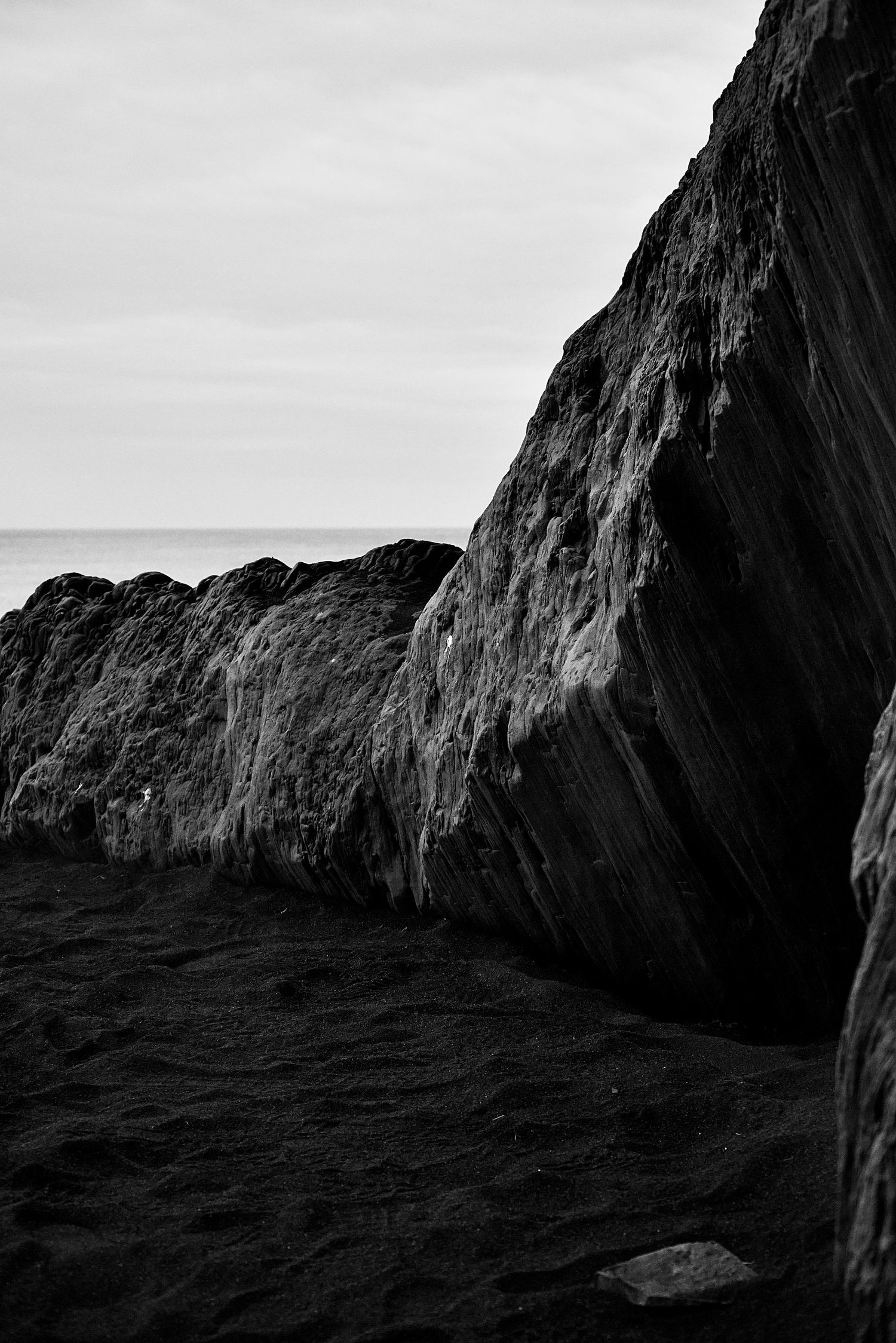 Black and white coastal rock formation with dark sand beach and ocean horizon in the background. Black sand beach in Iceland.