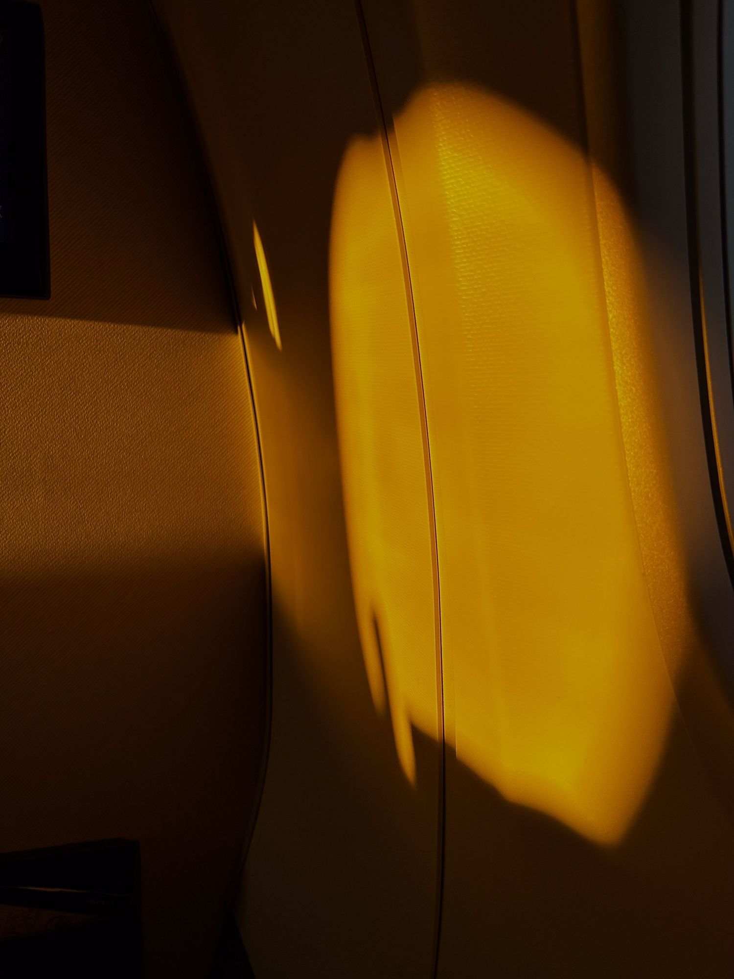Warm golden light casting an oval glow on a dark textured wall, creating a dramatic amber shadow effect.