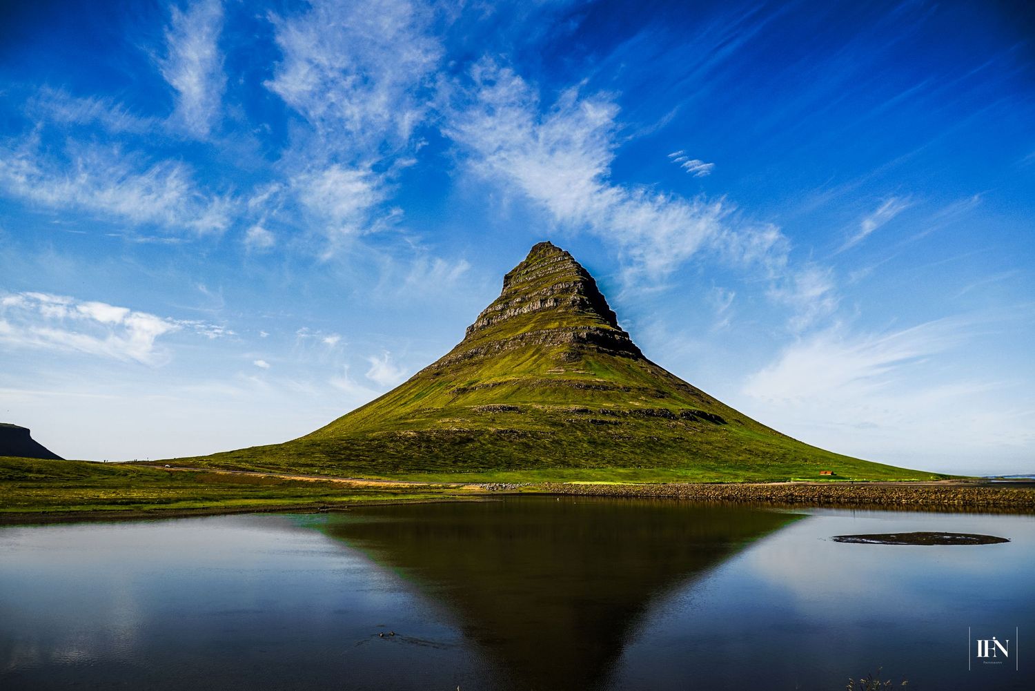Kirkjufell mountain reflected in calm water under blue sky in Iceland.