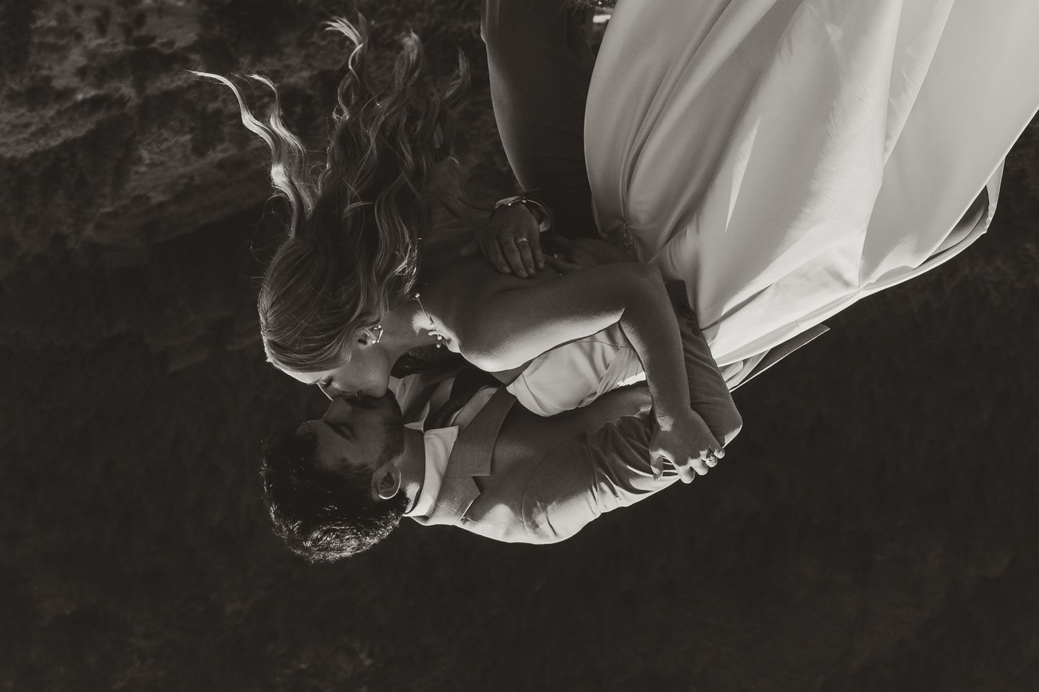 Black and white overhead shot of couple in wedding attire sharing an intimate moment on rocky ground.