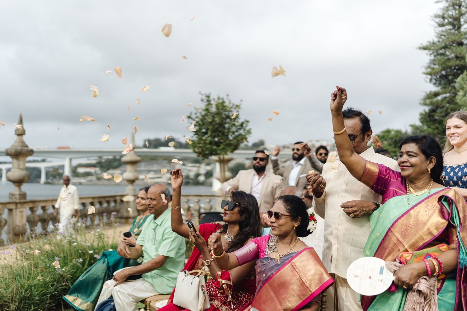Festive outdoor wedding scene with guests throwing flower petals in celebration.