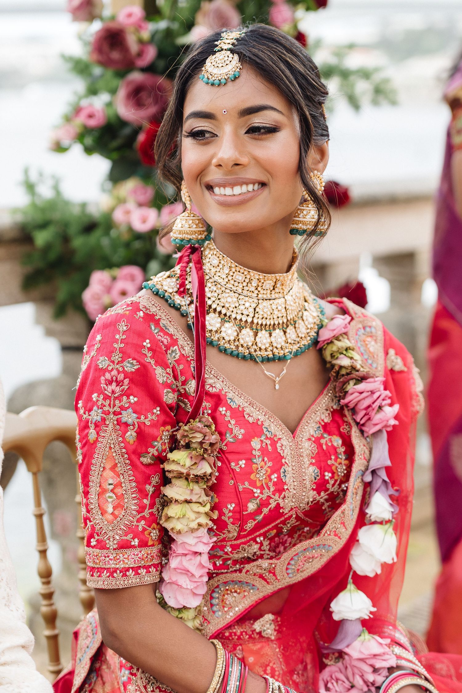 Traditional Indian bridal attire featuring a red embroidered lehenga with ornate gold jewelry and floral accessories.