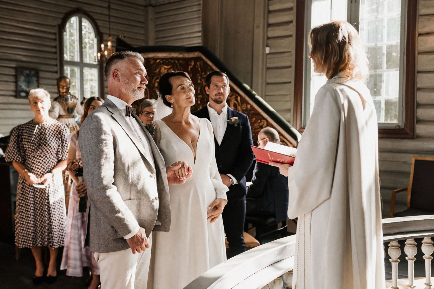 A wedding ceremony unfolds in a traditional church with white walls and elegant architectural details.