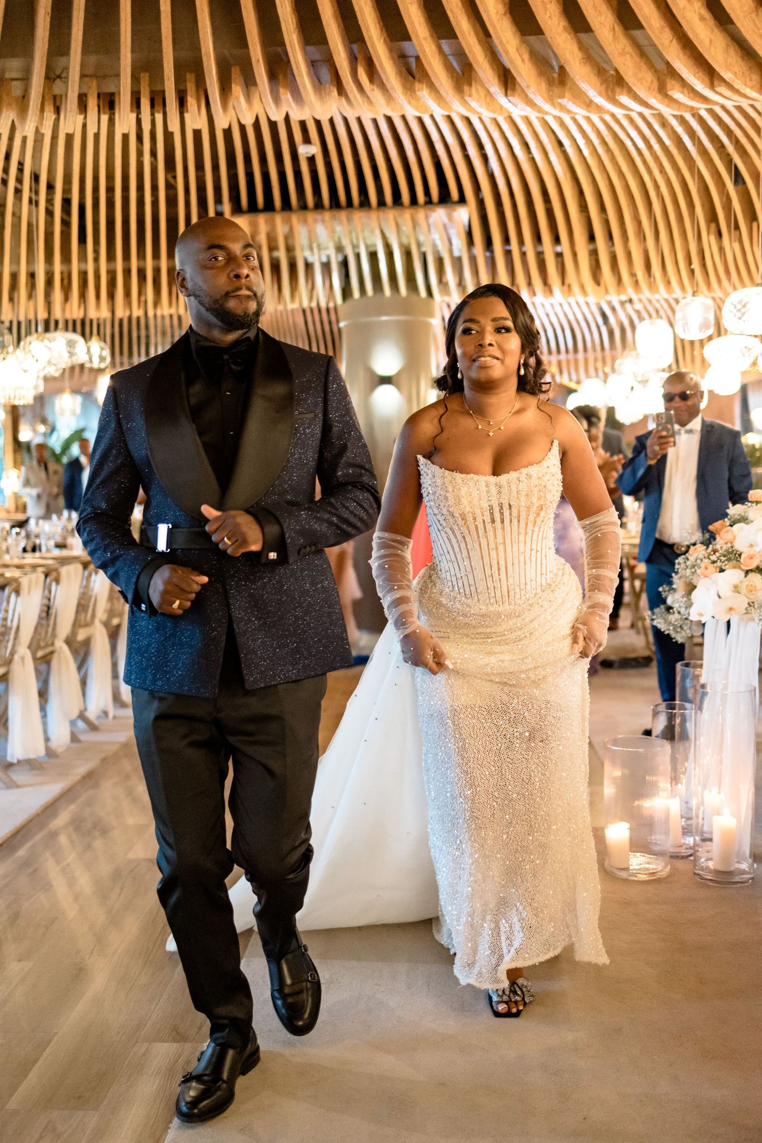 Couple walks through an elegant reception venue with wooden beam ceiling and chandeliers.