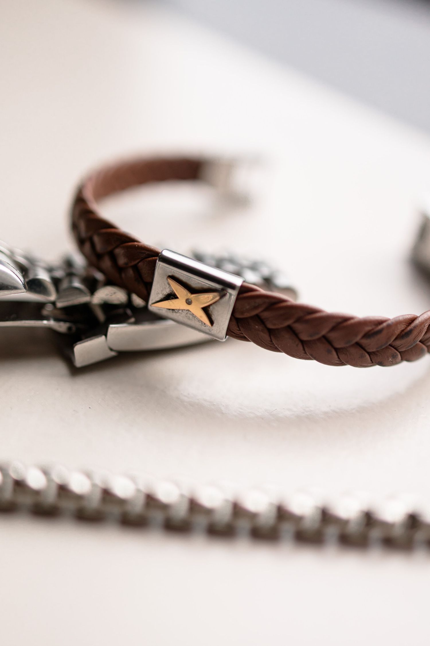 Close-up view of a brown leather bracelet with braided details against a white background.