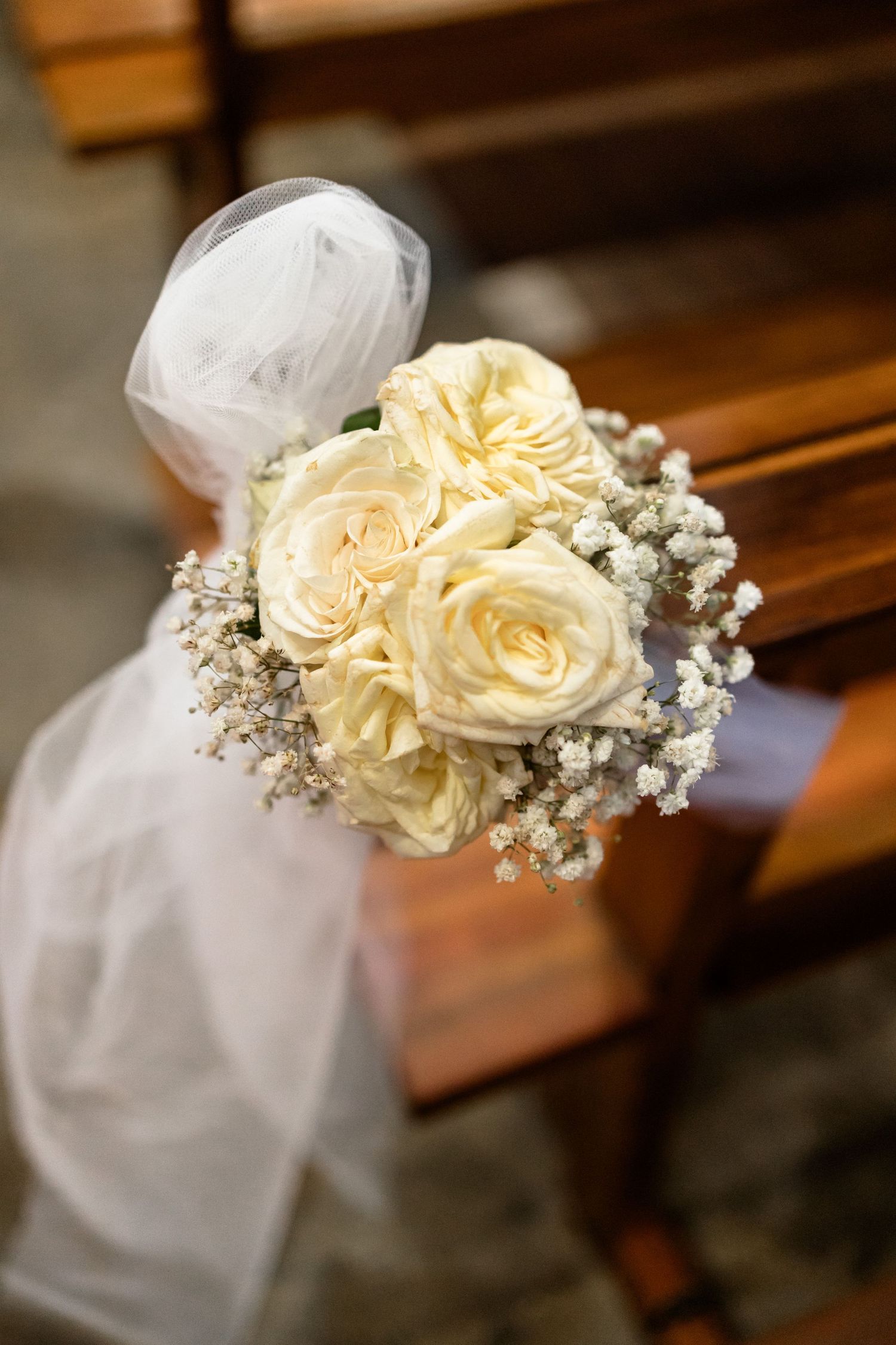 Elegant church pew decorations featuring cream roses and baby's breath with white tulle bows.
