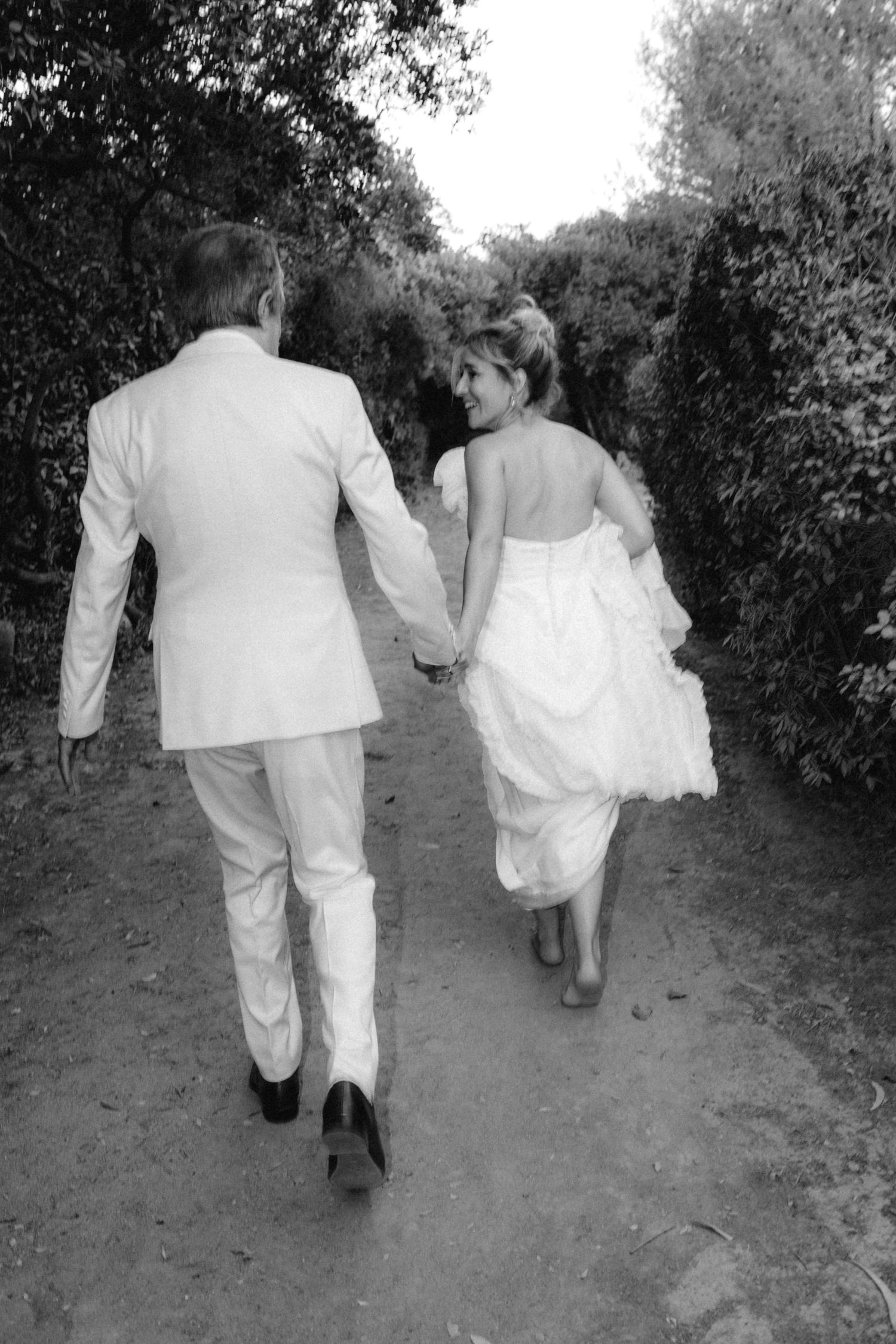 Black and white photo of a couple walking down a garden path after their wedding ceremony.