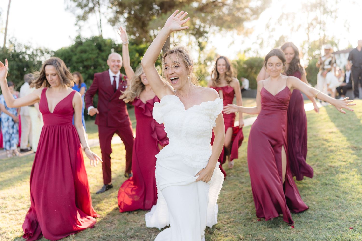 Joyful dancing at outdoor wedding with burgundy bridesmaid dresses and white bridal gown.