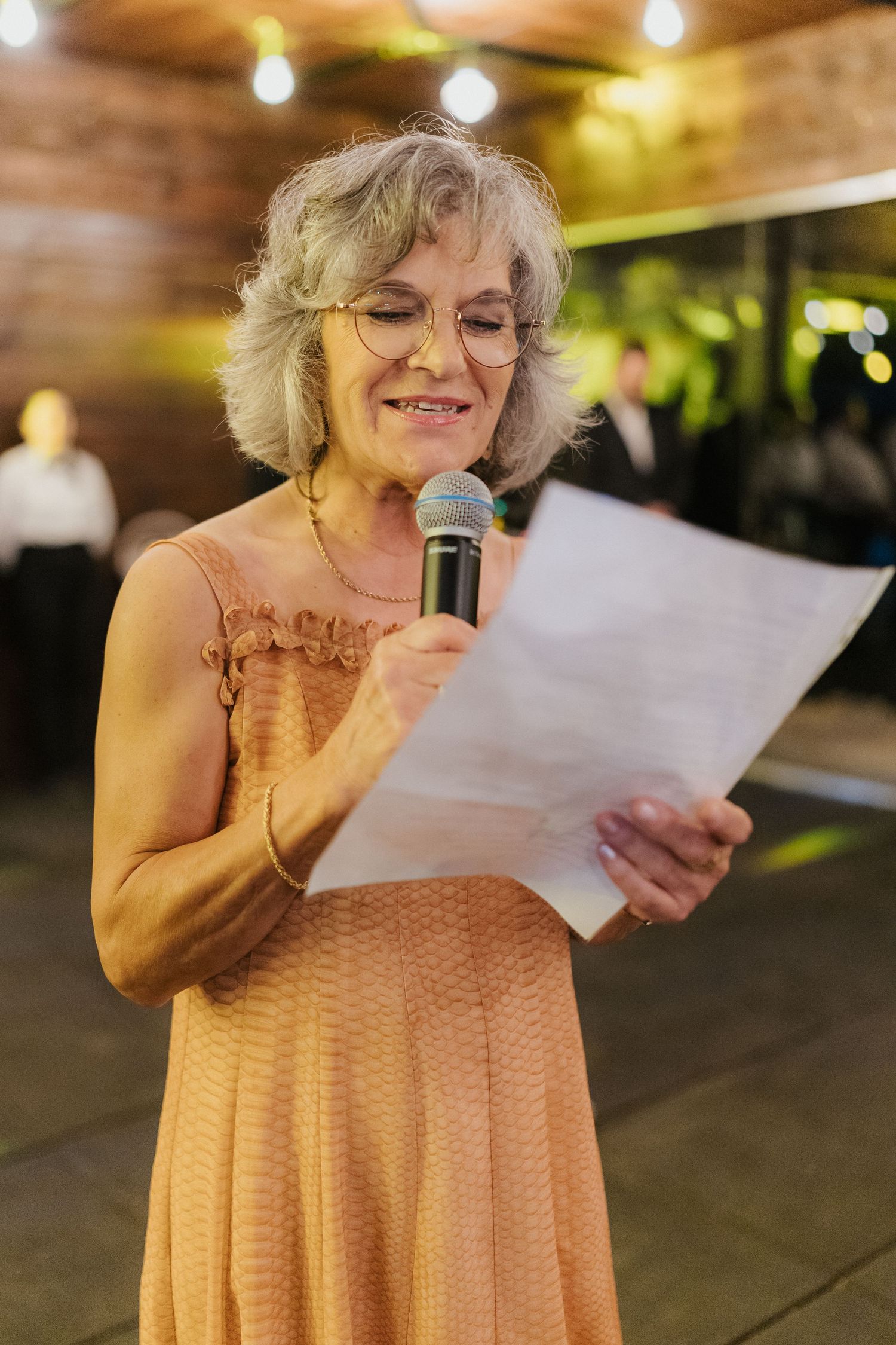 Person in peach dress giving speech at evening celebration.