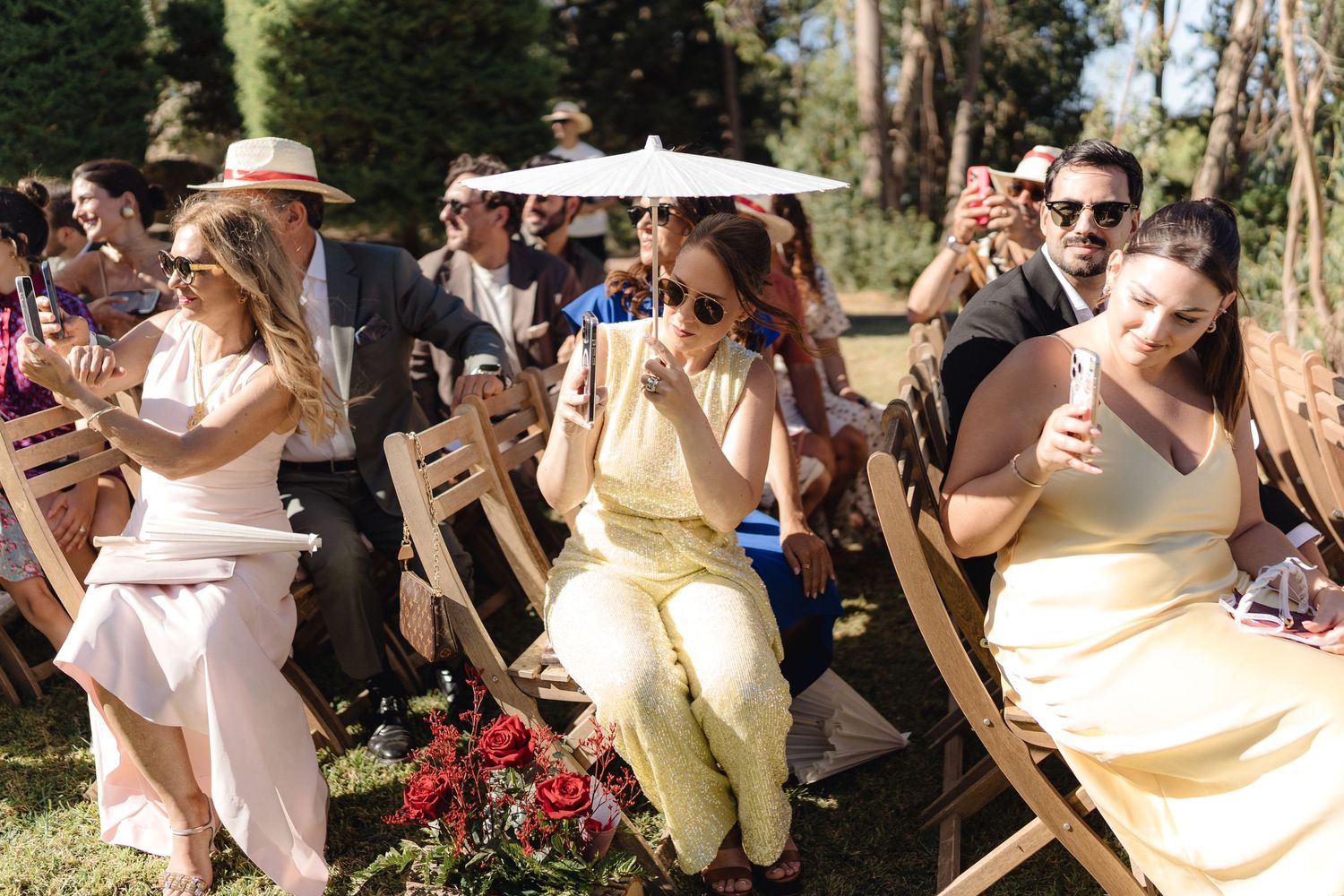 Wedding guests seated in wooden chairs outdoors watch ceremony with emotional expressions.
