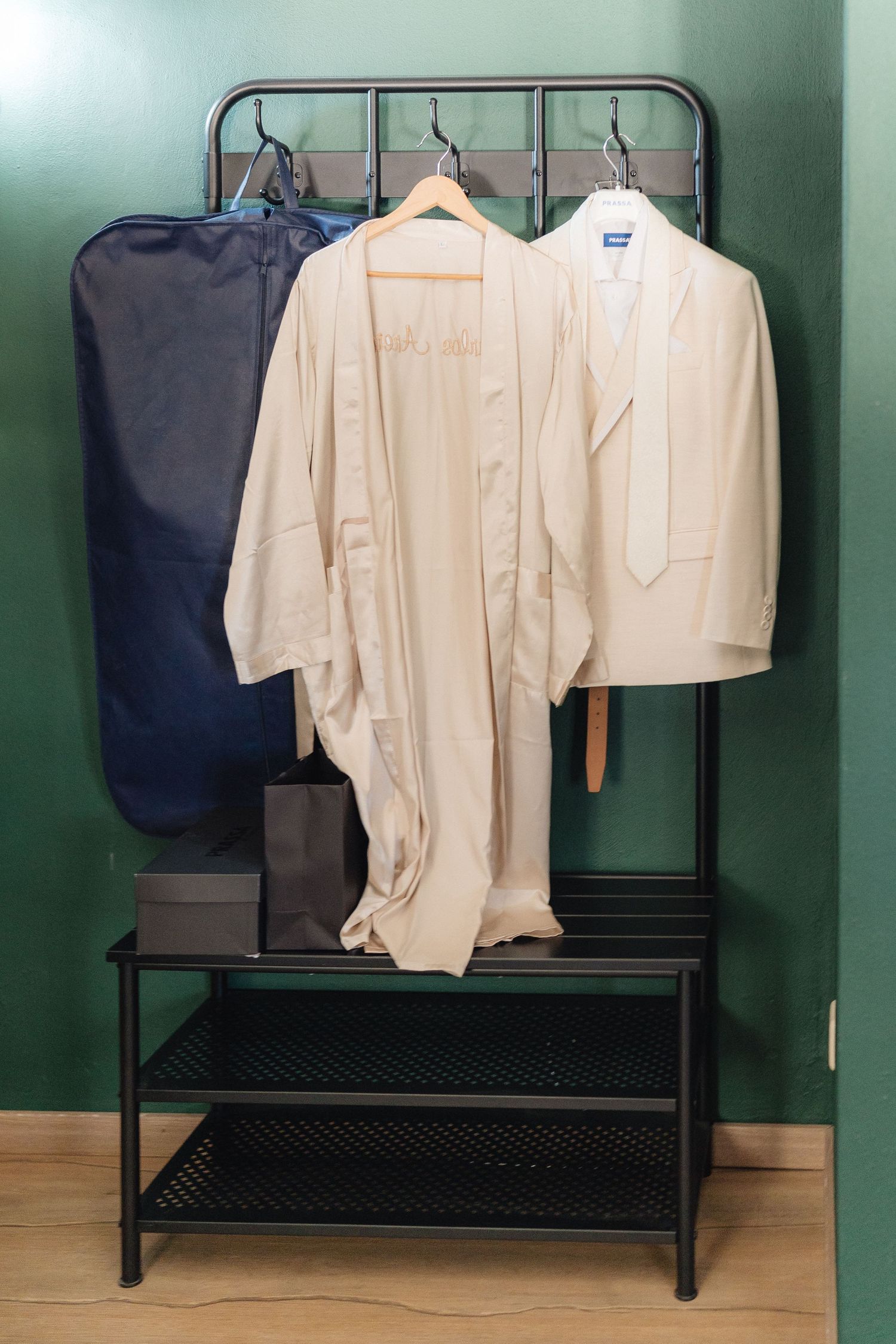 Cream colored formal suits hanging on black metal rack against mint green wall.