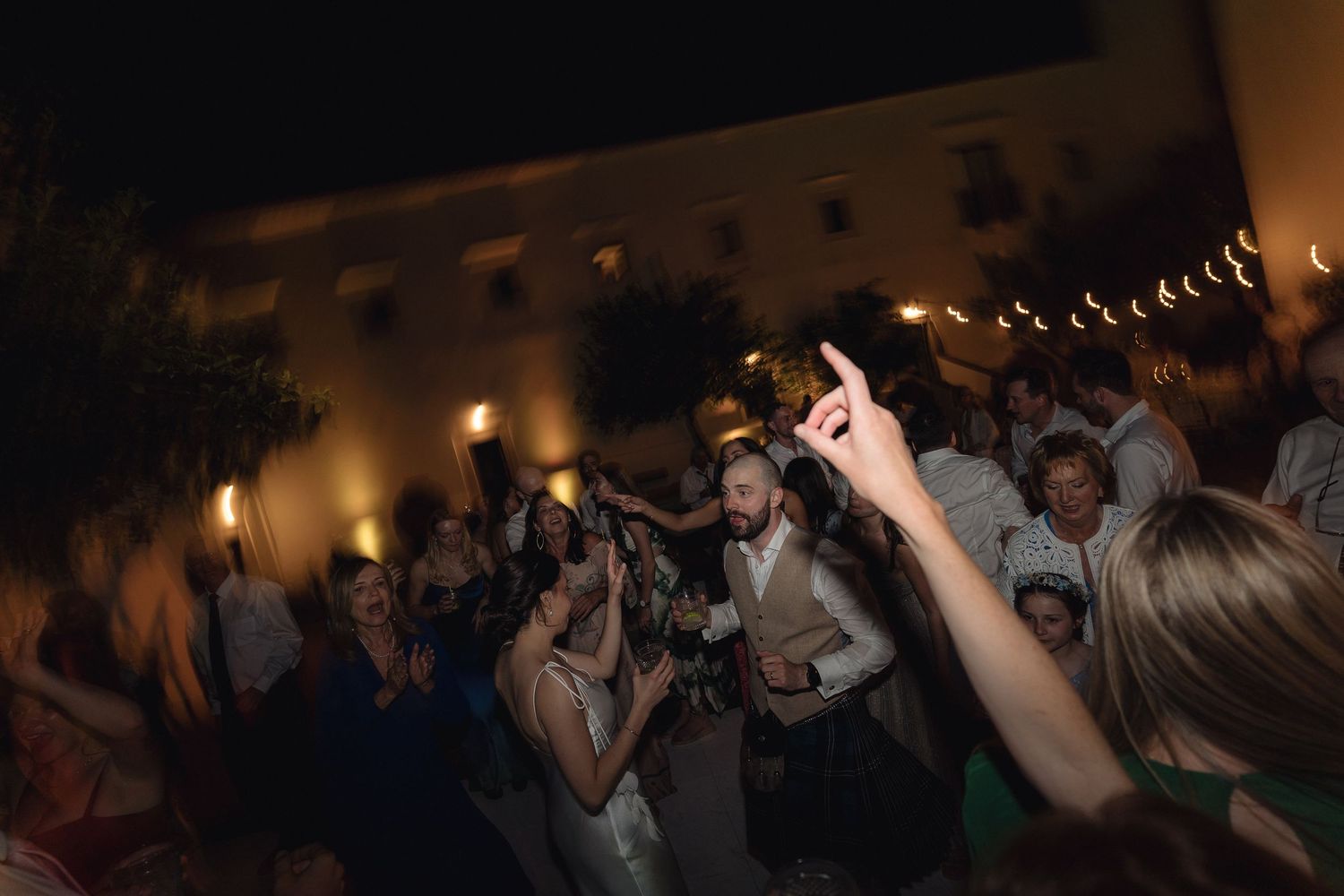 Indoor celebration with string lights and people dancing on a crowded floor.