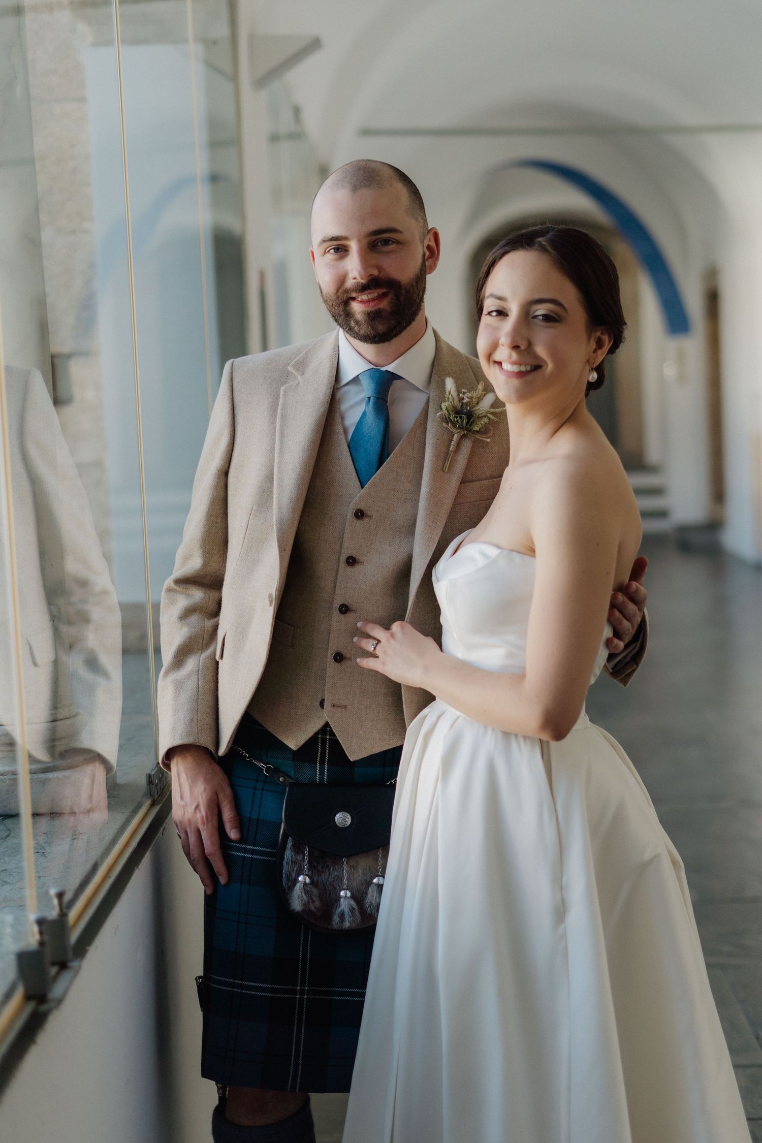 Couple laughs together in elegant white corridor with arched ceilings.