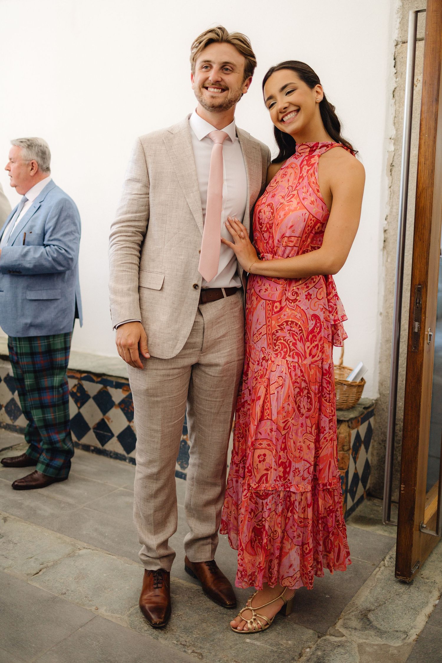 Wedding guests in formal attire posing against white walls and wooden doors.
