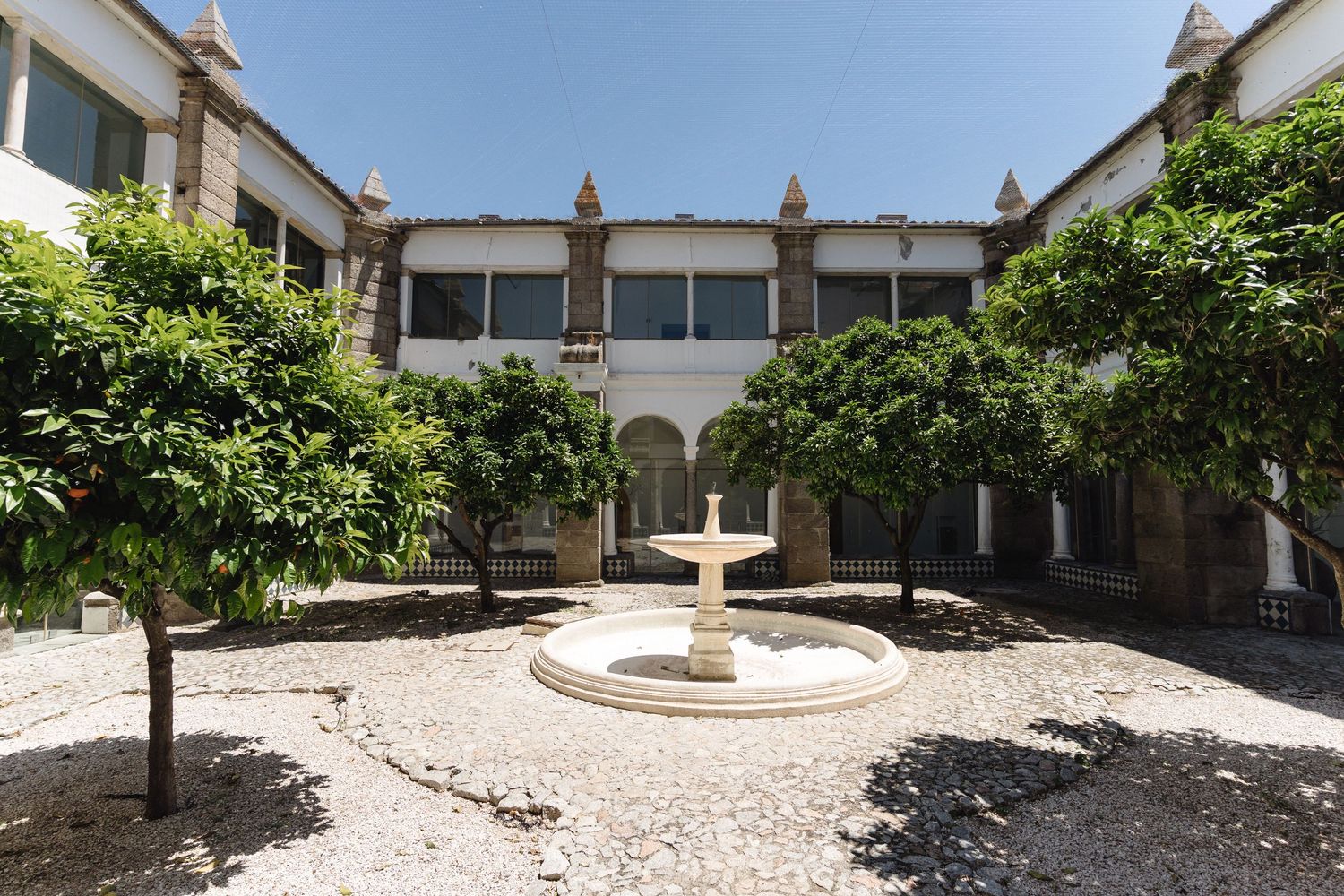 Tranquil monastery courtyard with white walls and stone cross centerpiece surrounded by landscaped grounds.