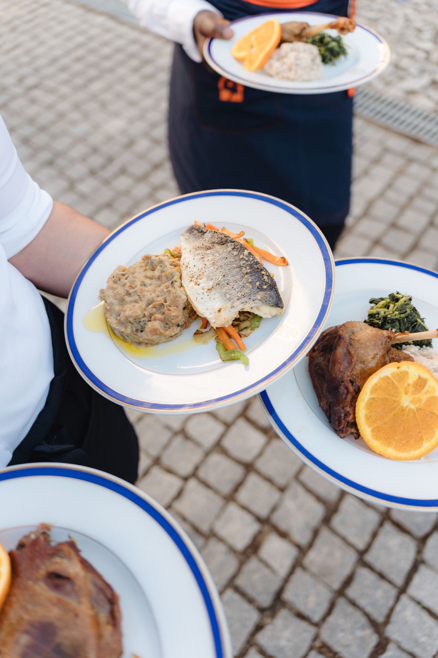 Multiple plates of elegantly served fish dishes with orange garnish on blue-rimmed plates.