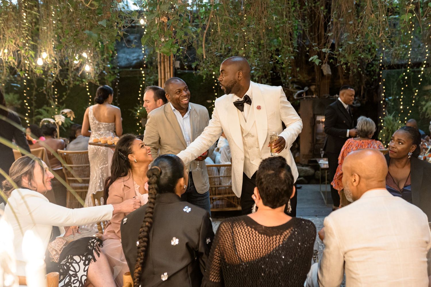 Guests dancing and celebrating at an elegant wedding reception under twinkling lights and greenery.