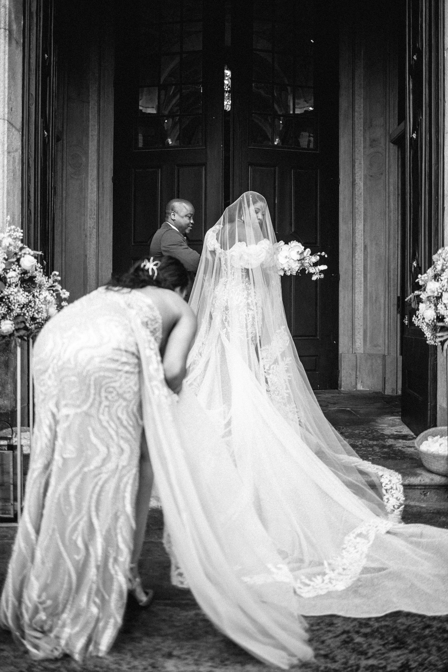 A black and white photo capturing the back of a bride's flowing lace train and veil.