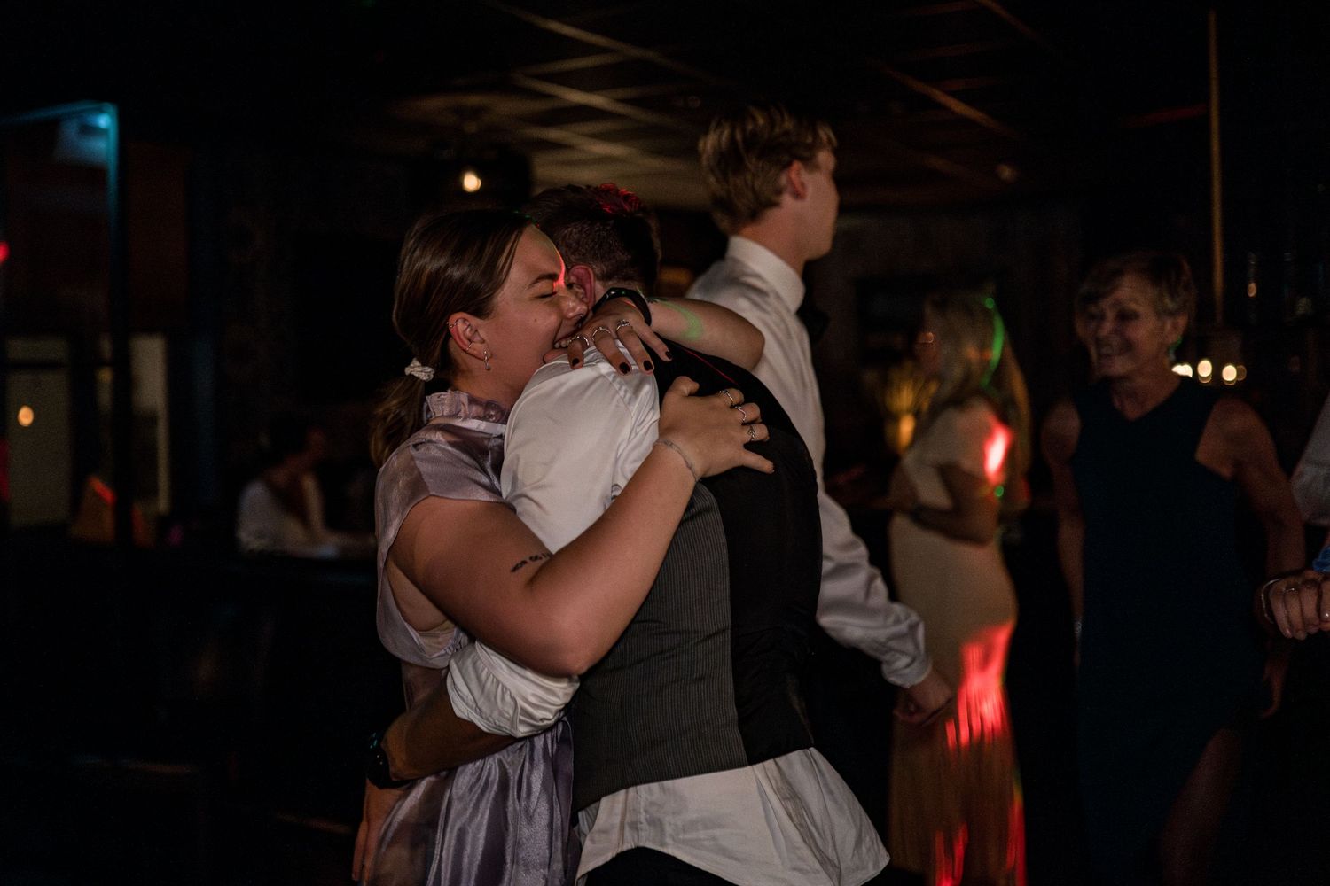 People dancing and embracing in a dark venue with atmospheric lighting.