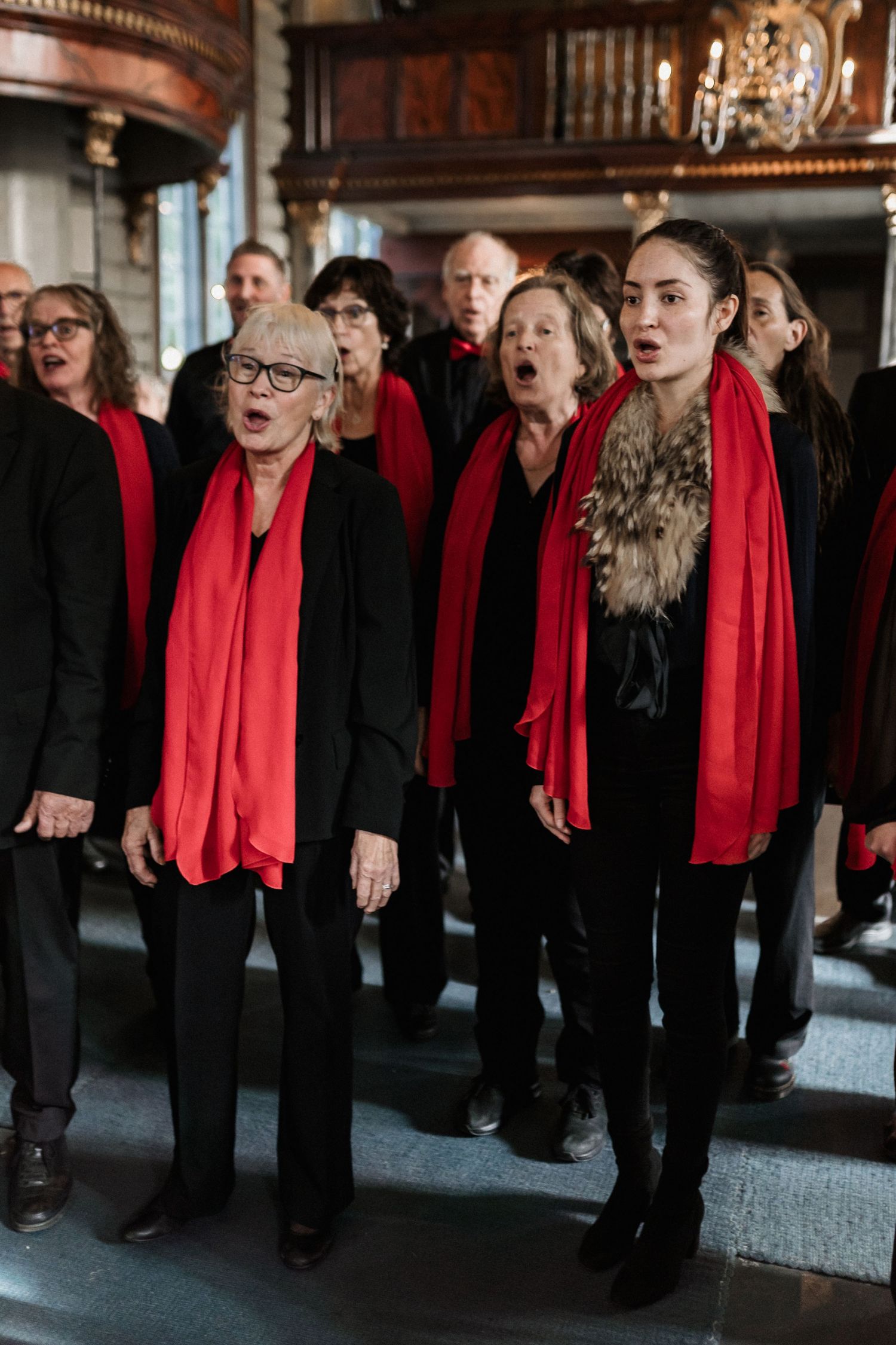 Choir members in black attire with bright red scarves performing in a traditional church setting.