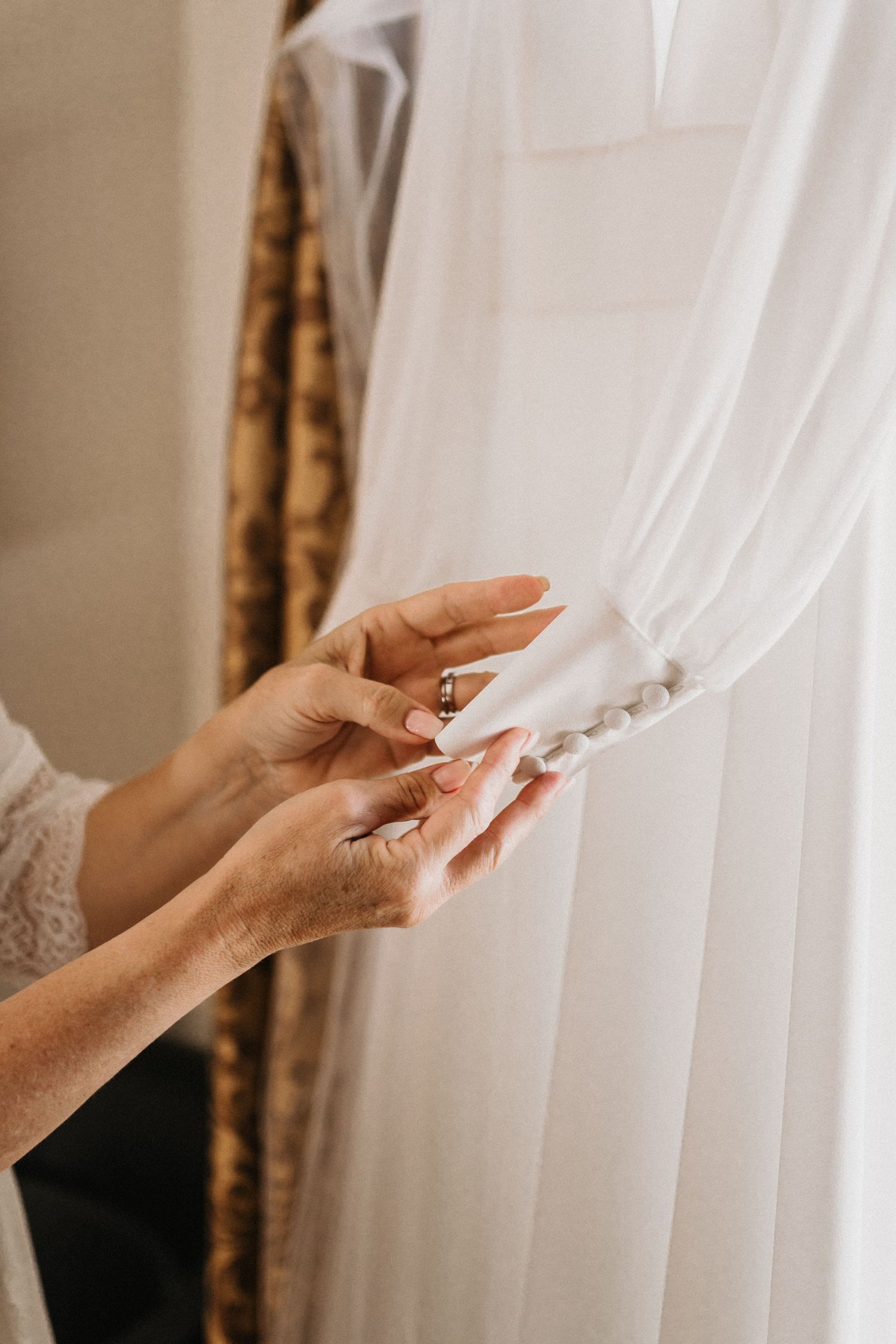Delicate hands gently touching sheer white curtains in soft natural light.