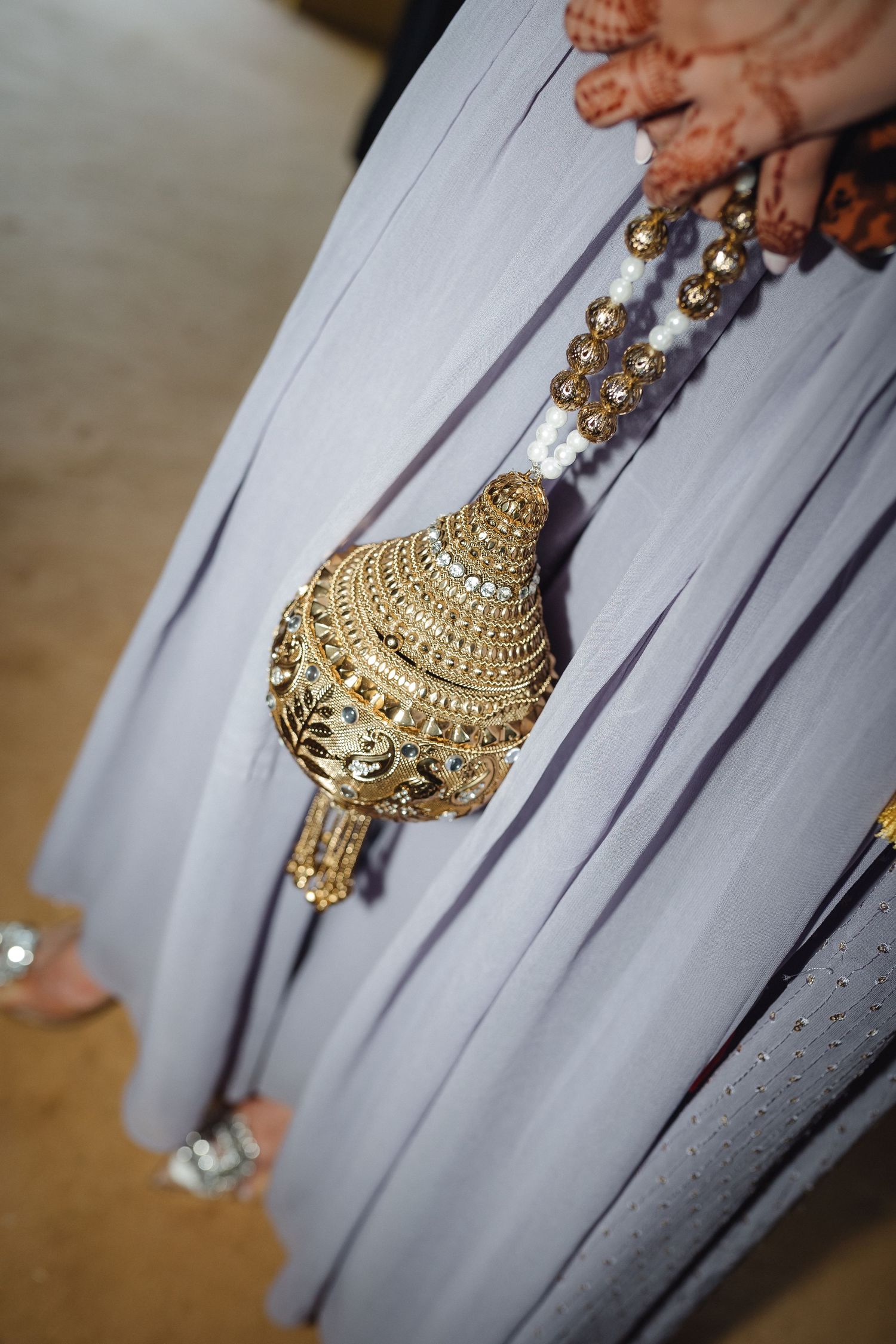 Ornate gold Indian wedding kalira with intricate traditional designs hanging against flowing gray fabric.
