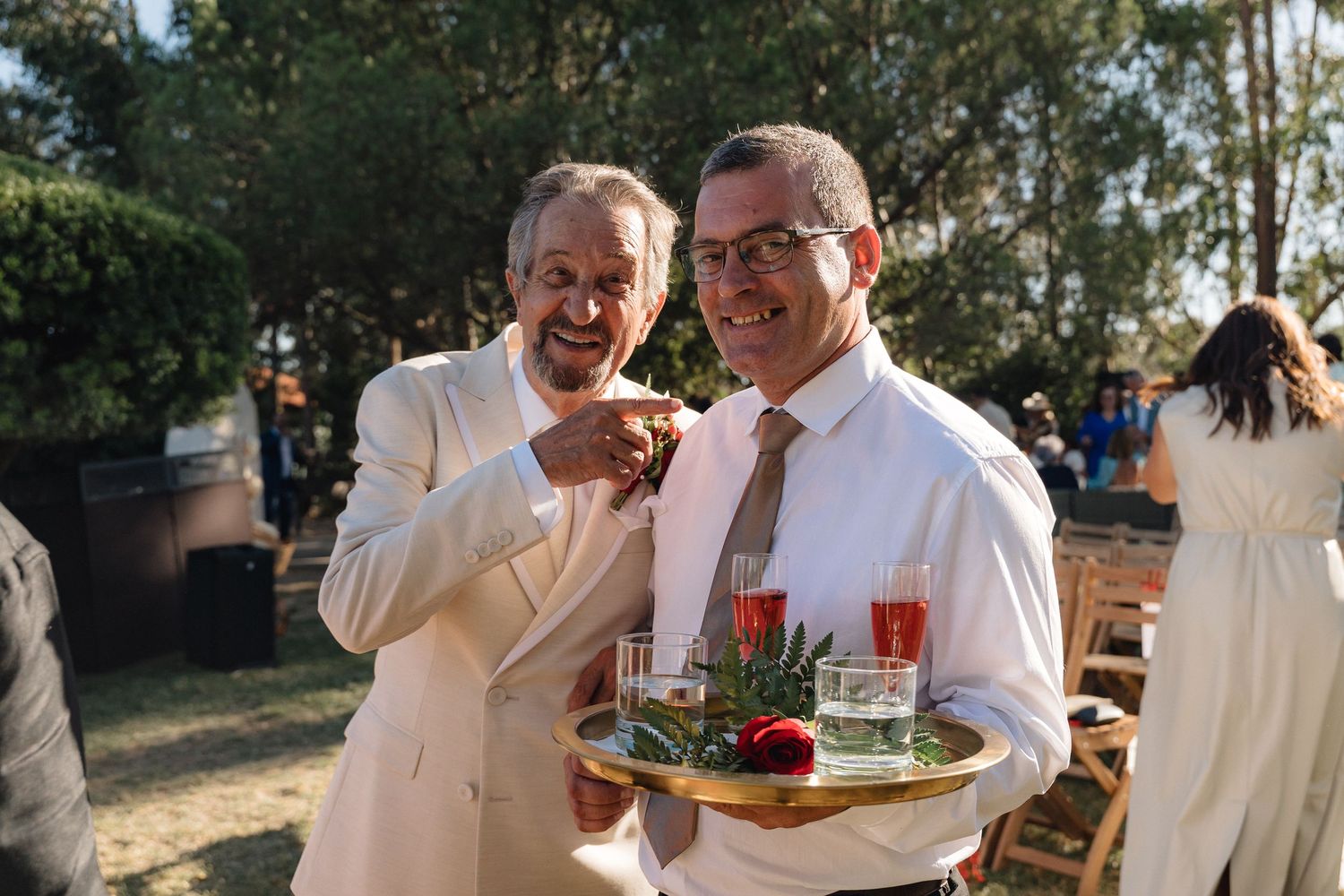 Two guests in formal attire share drinks and conversation at an outdoor event.