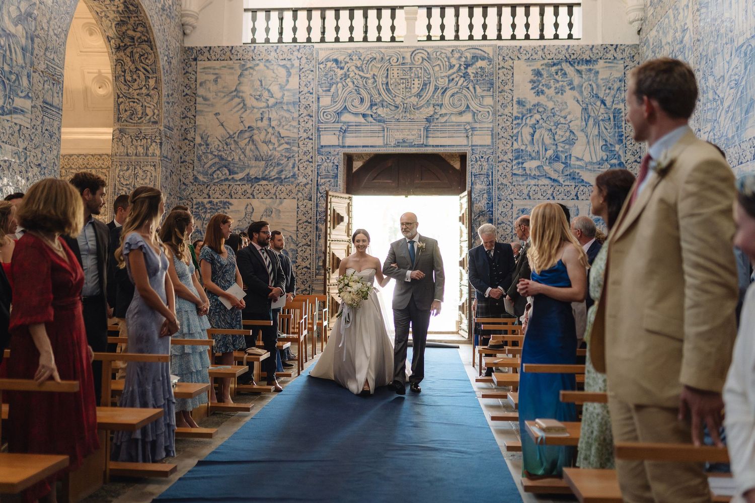 Wedding ceremony in a Portuguese chapel featuring dramatic blue and white tiled walls and wooden pews.