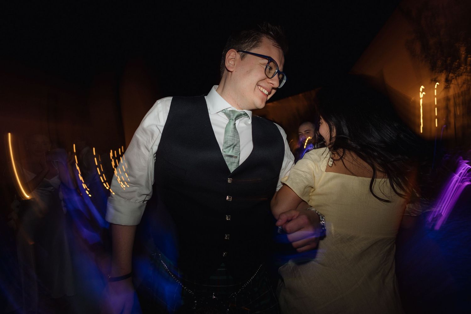 Party guests dancing and celebrating in a dark venue with colorful lighting effects.