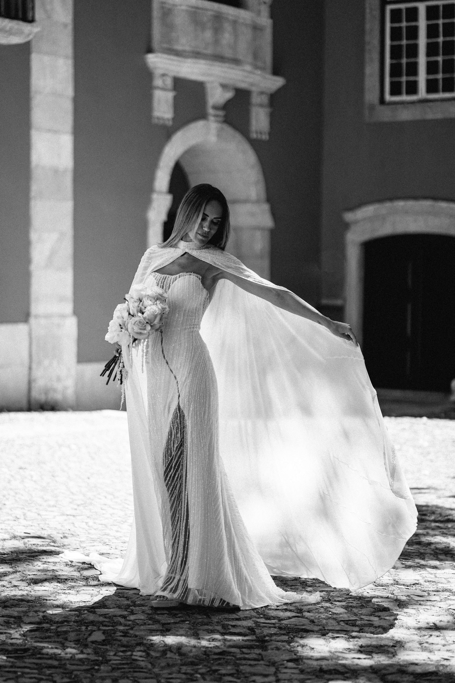 Black and white photo of flowing wedding dress movement in historic courtyard setting.