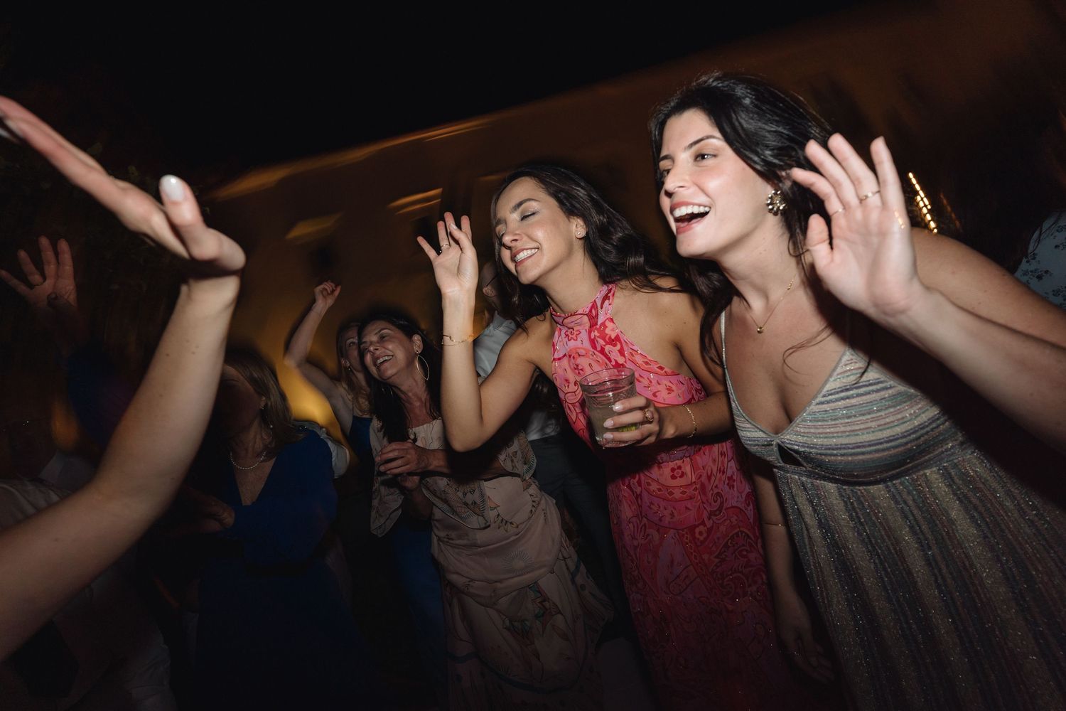 Wedding party dancing energetically under outdoor lighting at an evening celebration.