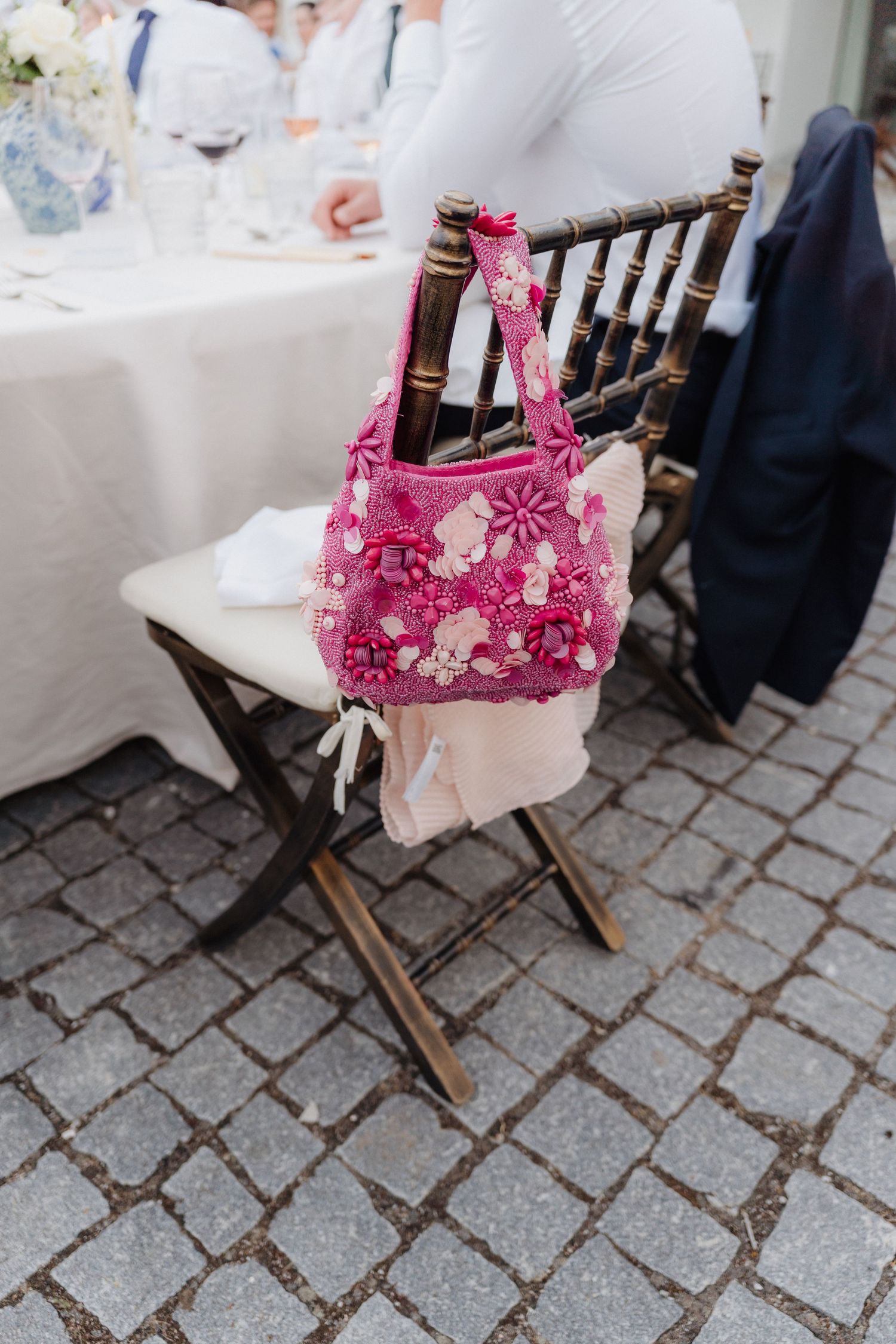 Pink floral cushion decorating a dark wooden folding chair on cobblestone ground.