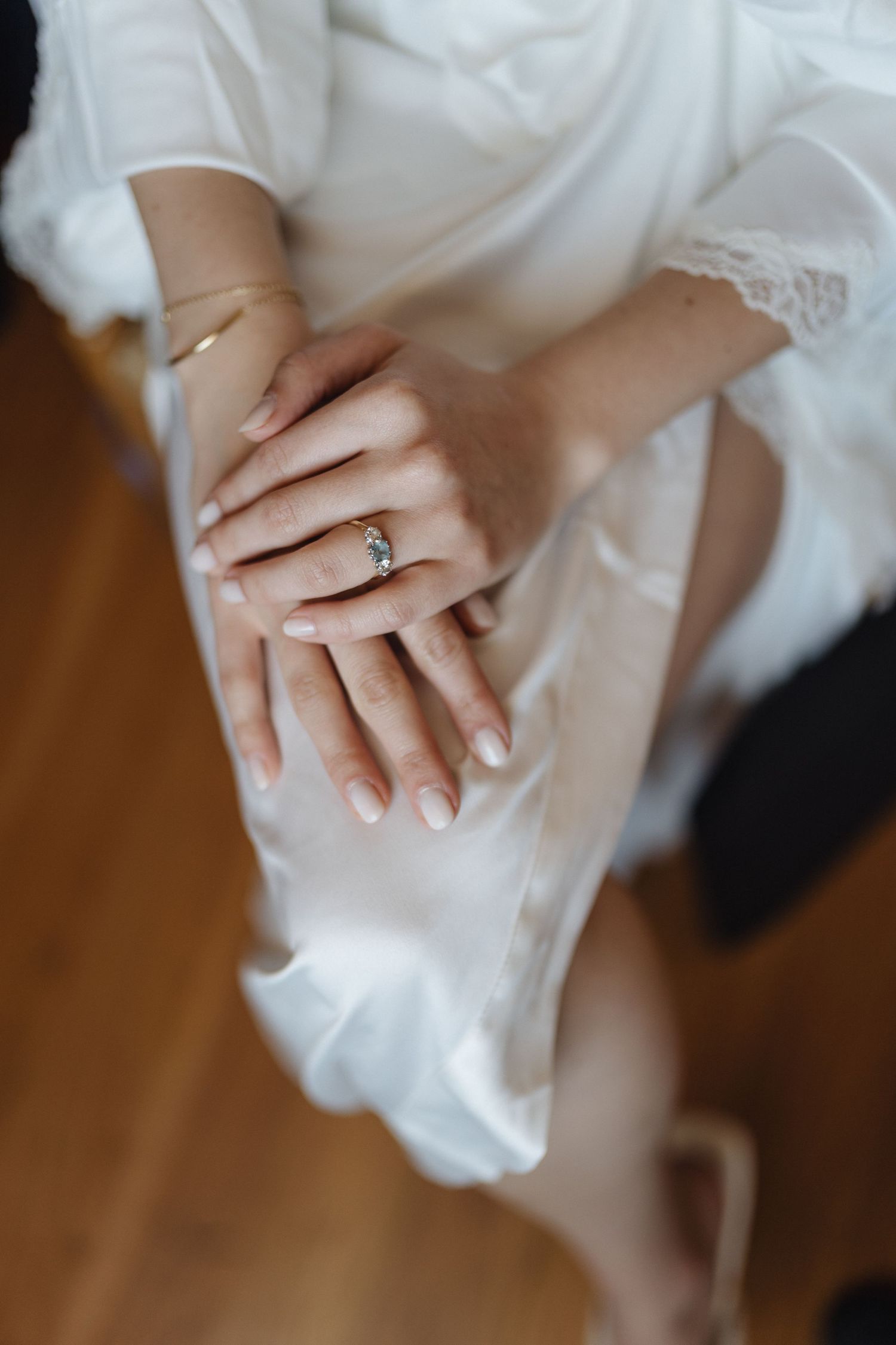 Detail shot of hands with engagement ring against white fabric.