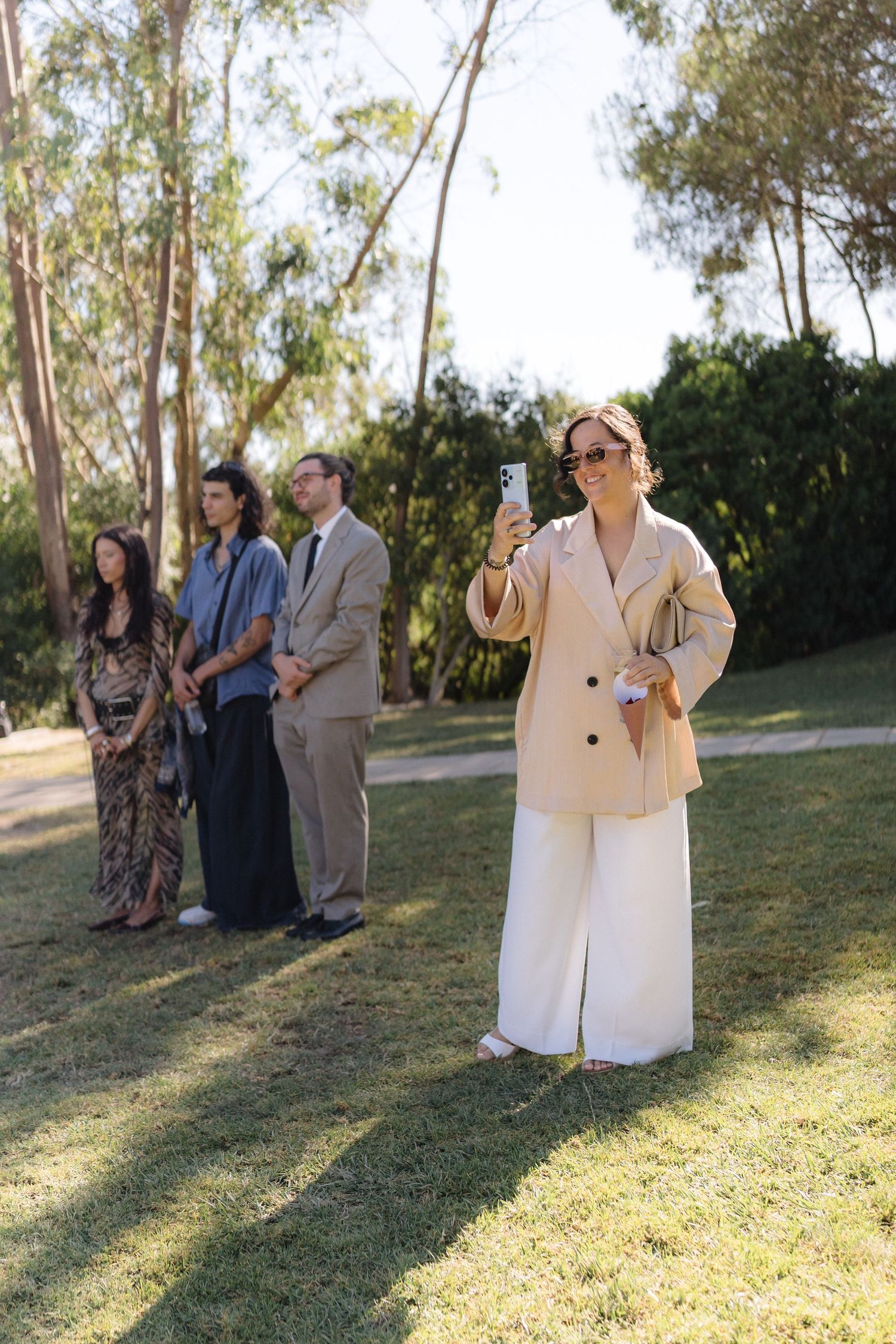 Wedding guests taking photos during outdoor ceremony among eucalyptus trees.