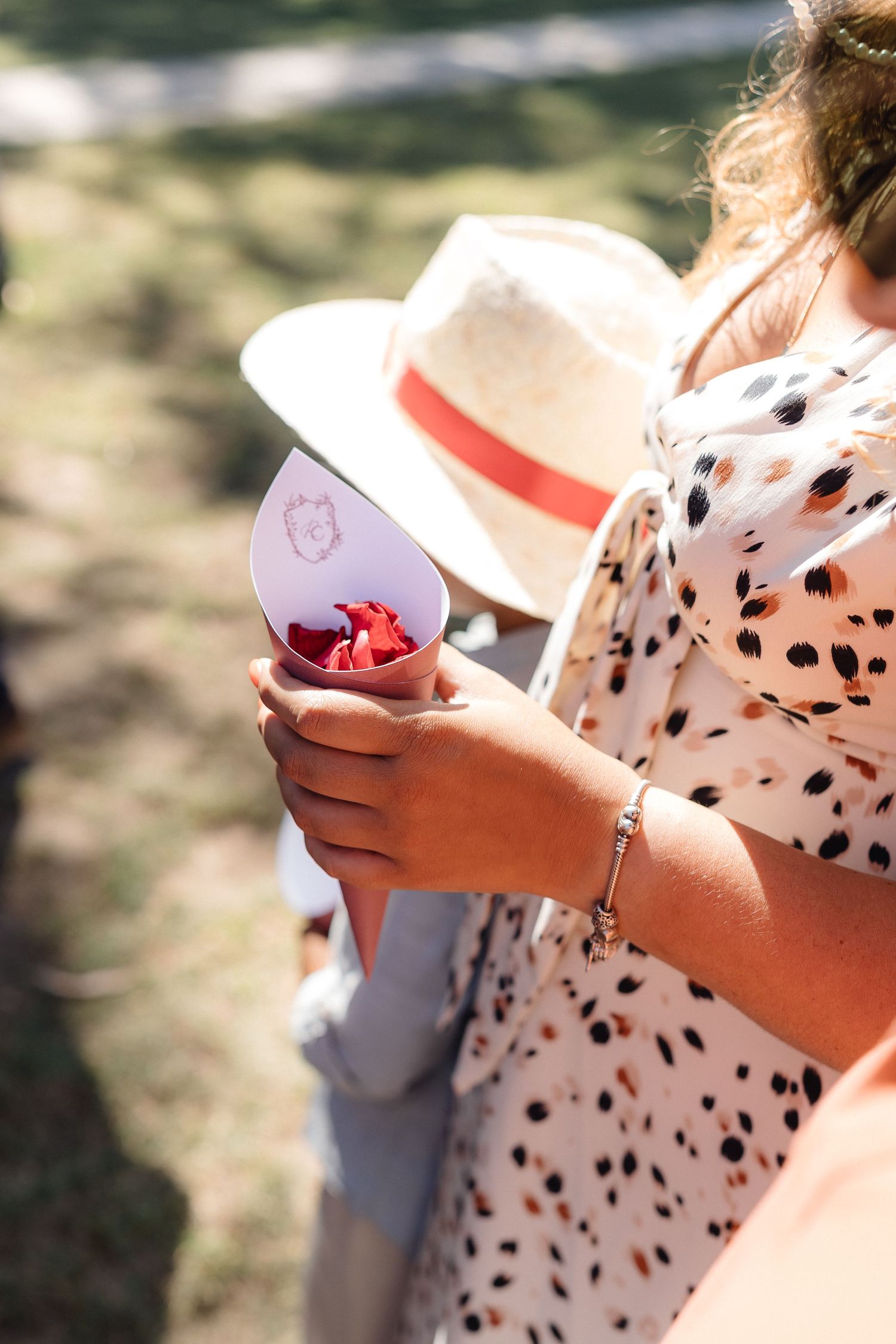 Close-up of hands holding a polka dot patterned dress and drink at an outdoor event.