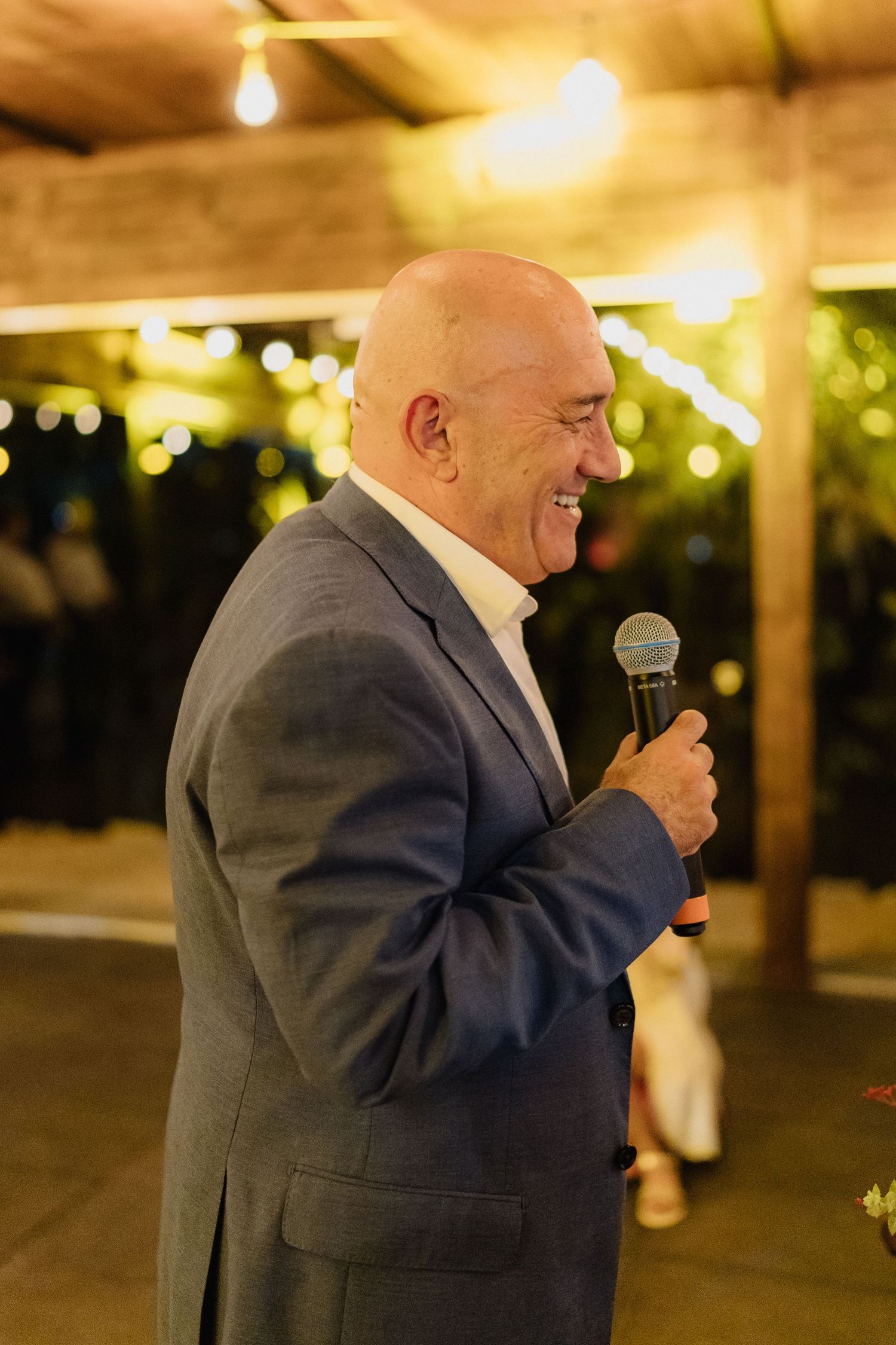 A speaker in a blue suit delivers a speech at an evening reception with warm lighting.