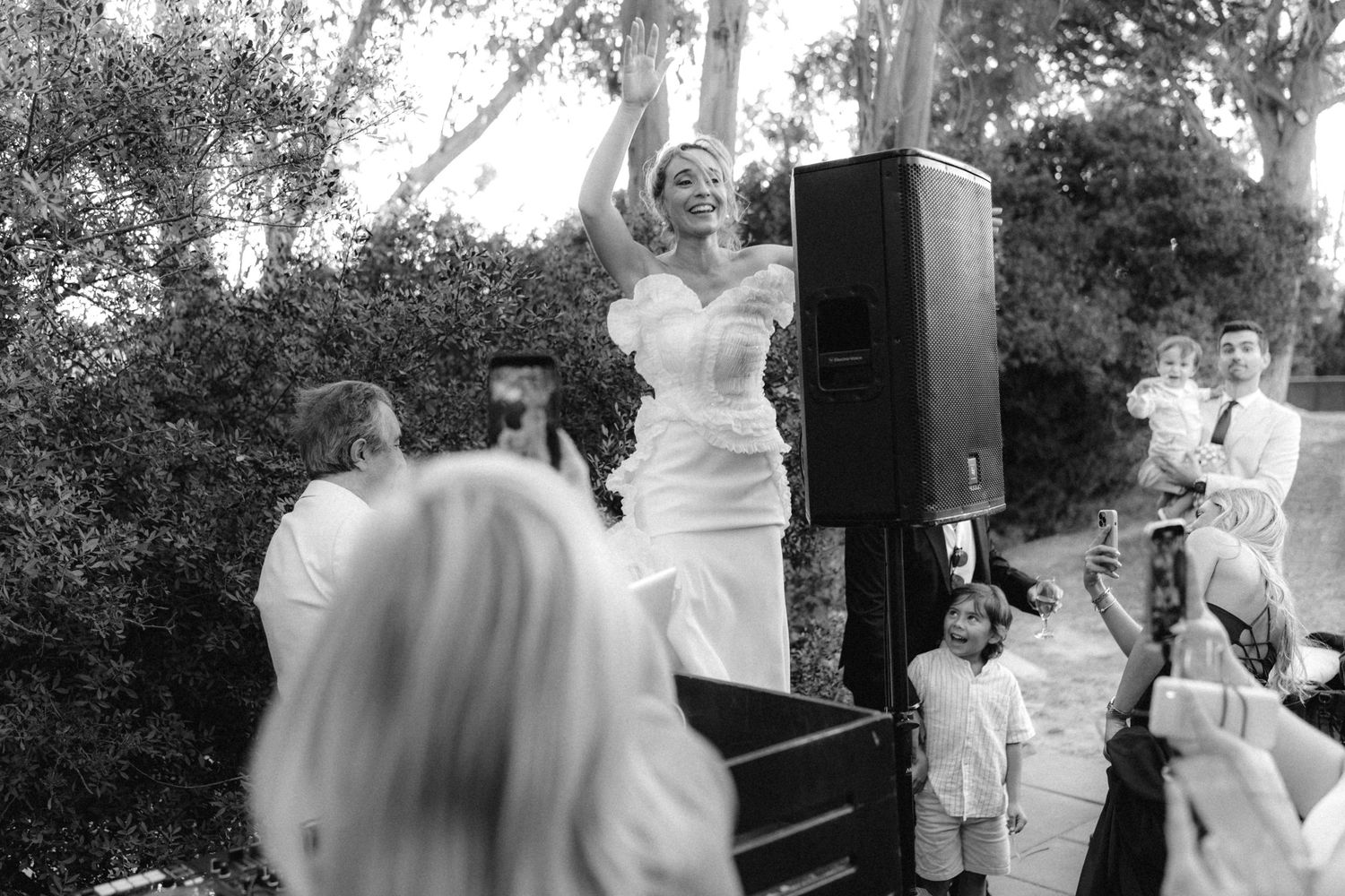 Wedding guests dancing and celebrating at an outdoor reception with joyful expressions.