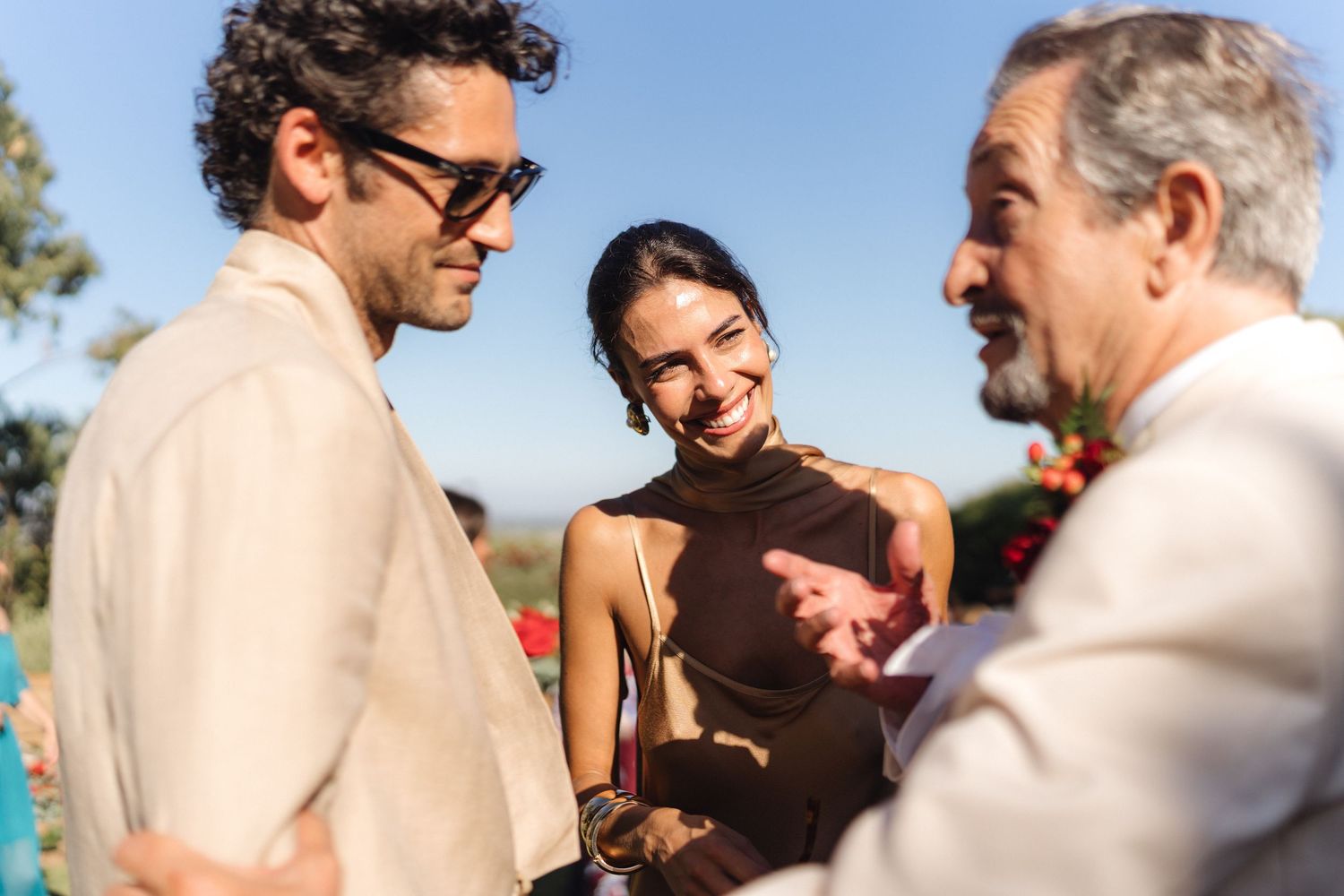 Wedding guests share emotional embraces during an outdoor celebration in warm sunlight.
