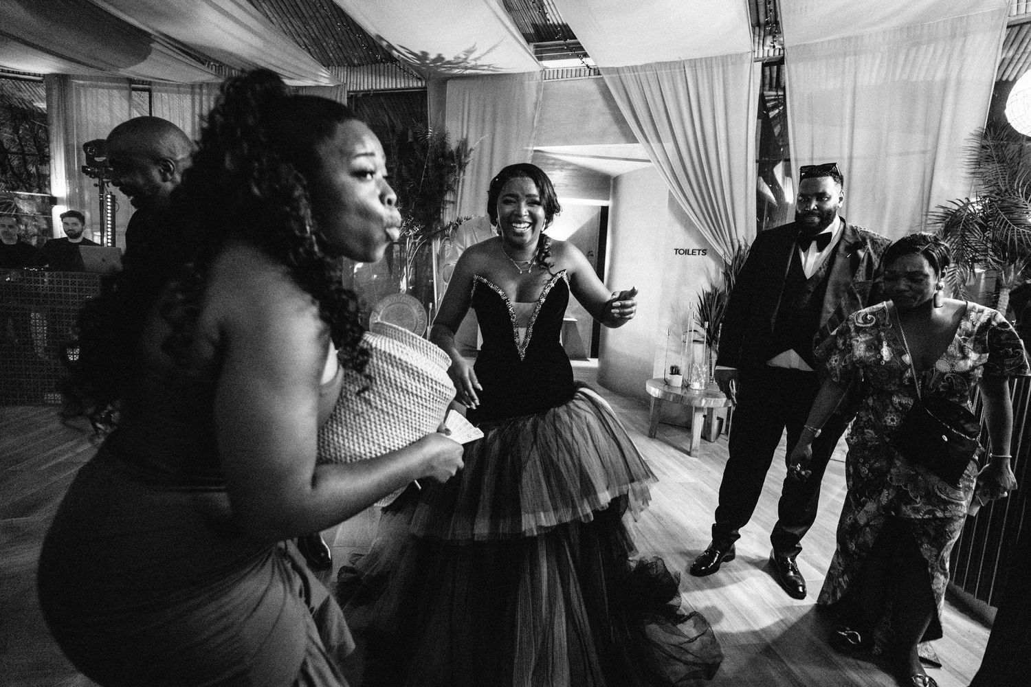A black and white photo of wedding guests dancing and celebrating at a reception.