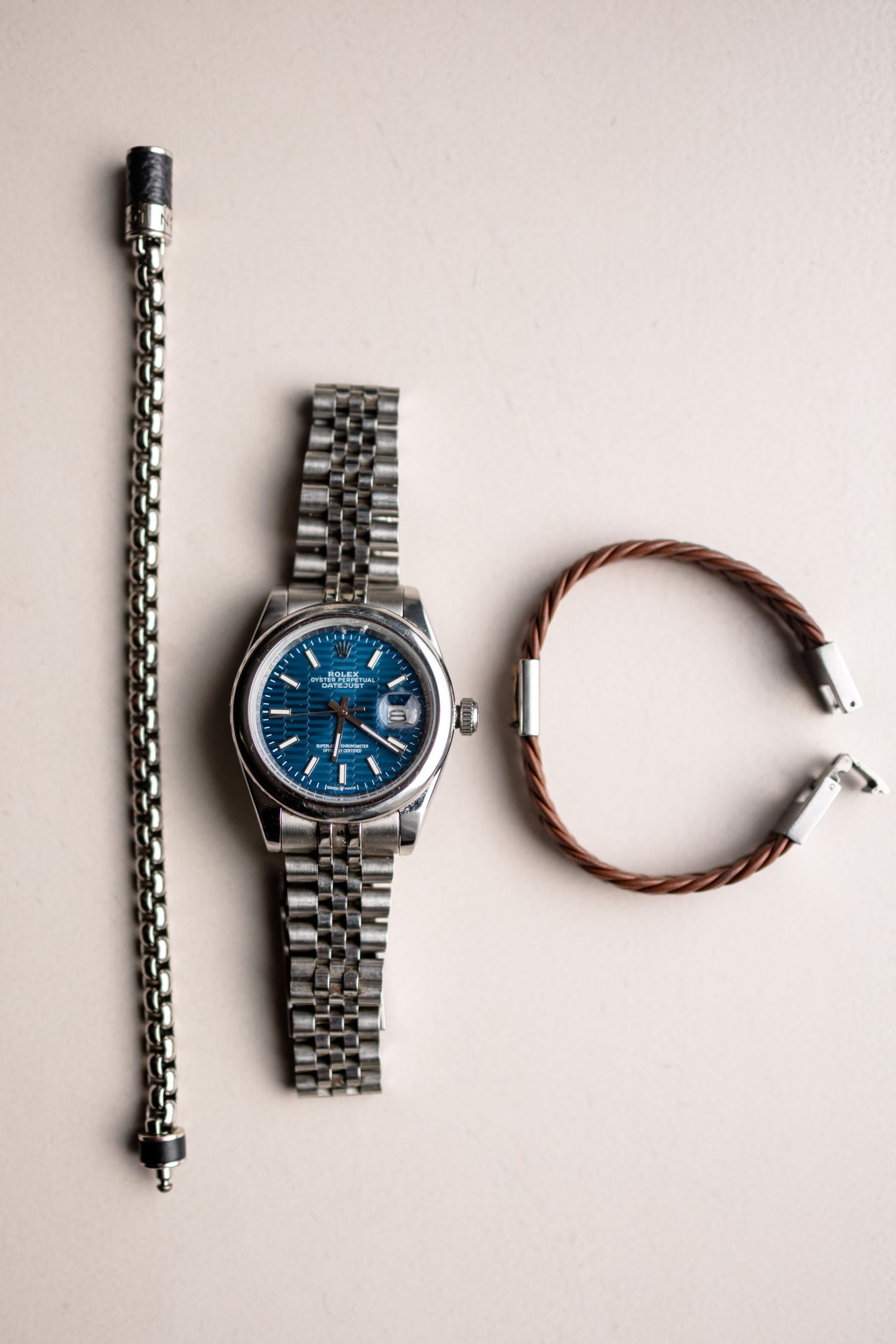 A silver watch with blue face and metal bracelet displayed alongside a leather accessory.