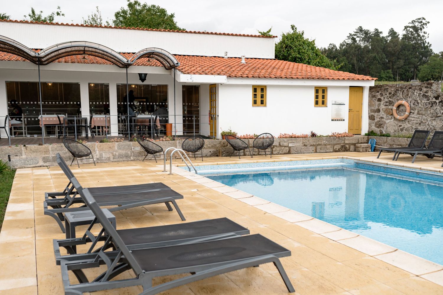 Modern swimming pool area with lounge chairs and umbrellas surrounded by white buildings and landscaping.