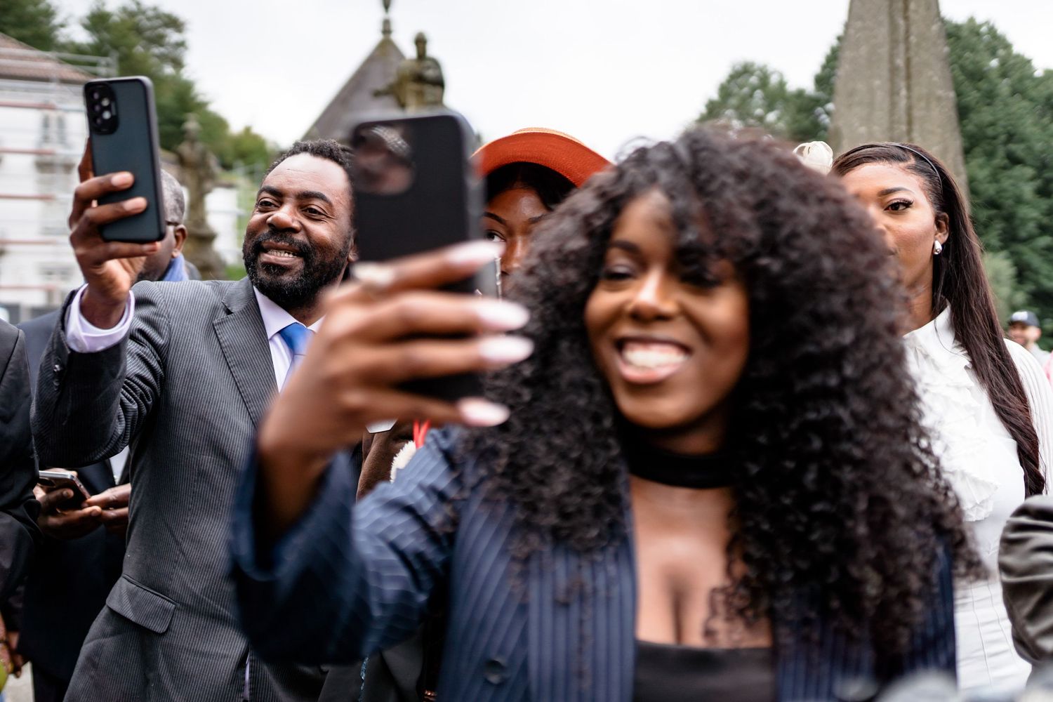 Wedding guests take selfies and photos outside while celebrating.