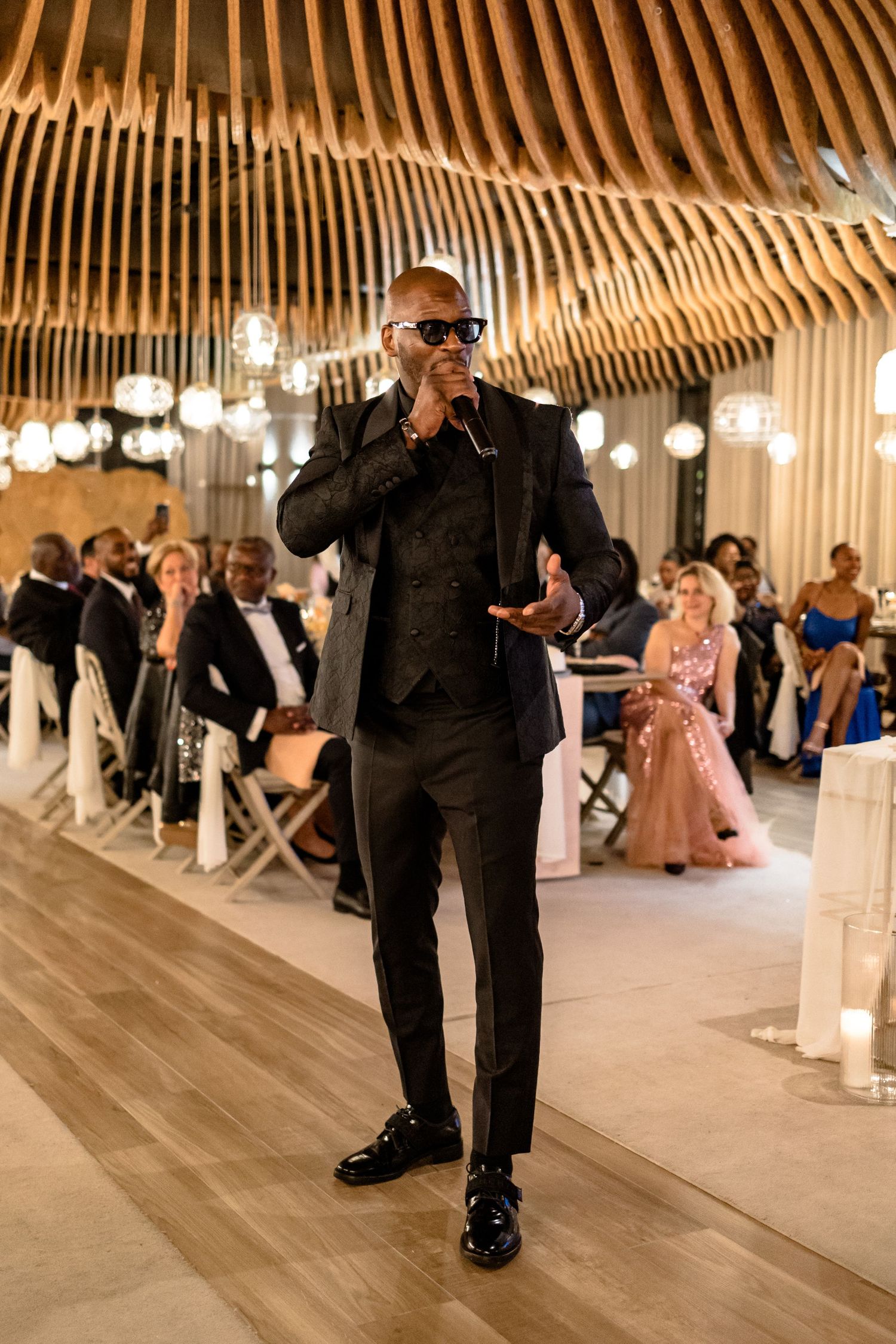 Guests dancing at a wedding reception under wooden beam architecture and pendant lighting.