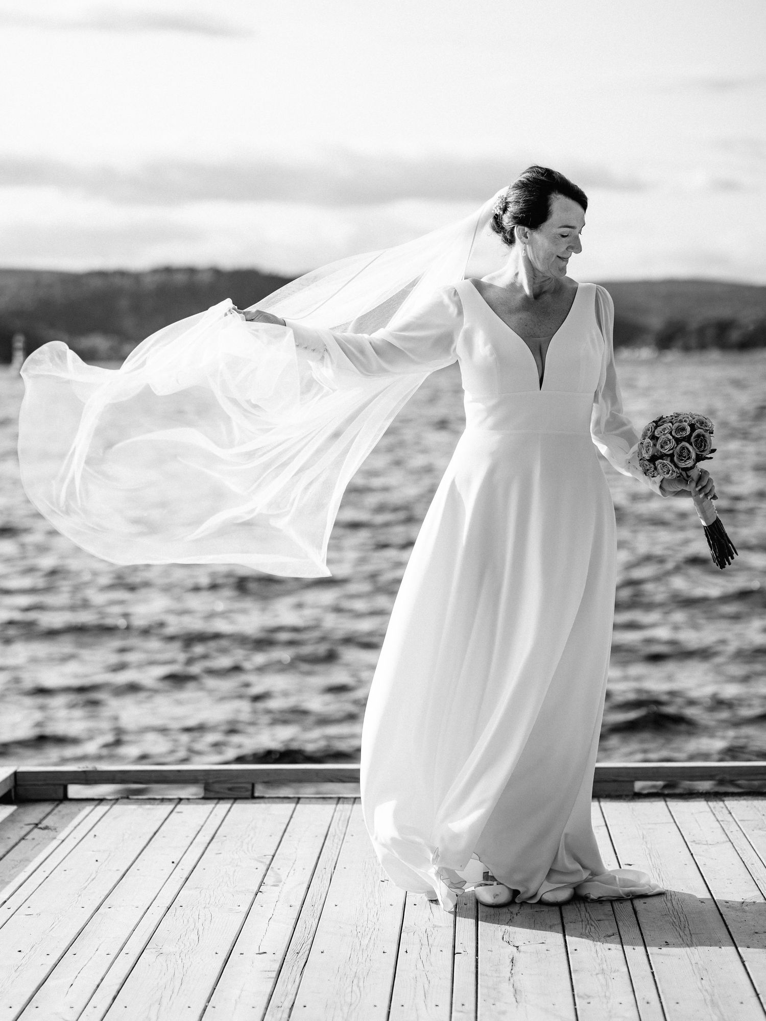 Artistic black and white series of a flowing white dress against a waterfront backdrop.