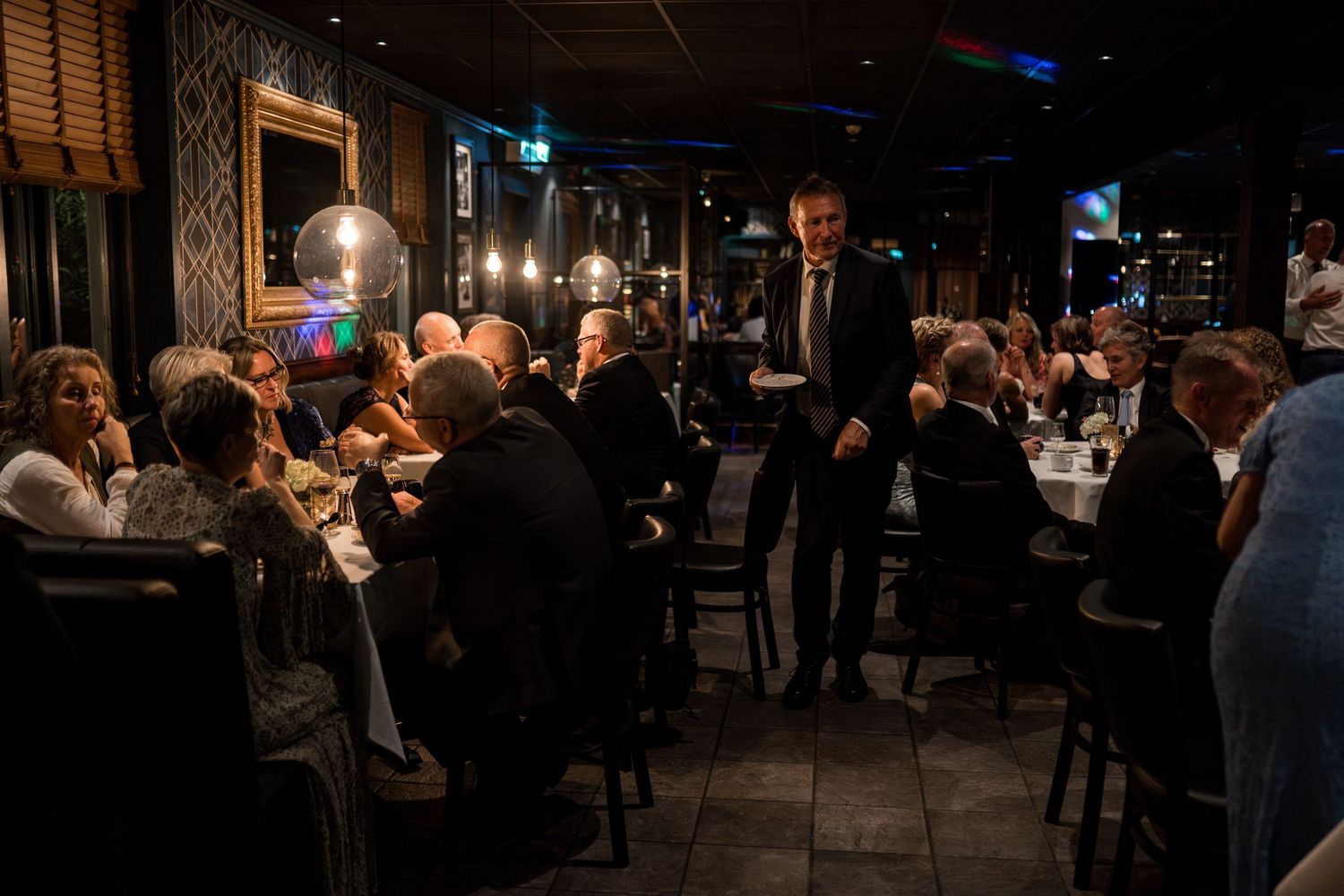 Dimly lit restaurant interior with guests dining at multiple tables in an elegant setting.