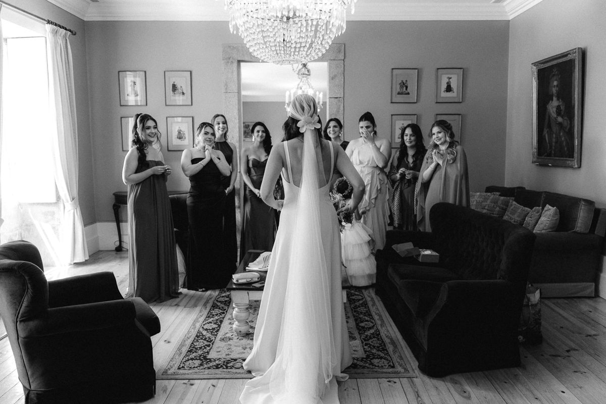 Wedding party gathered in elegant room with chandelier and formal portraits on walls.