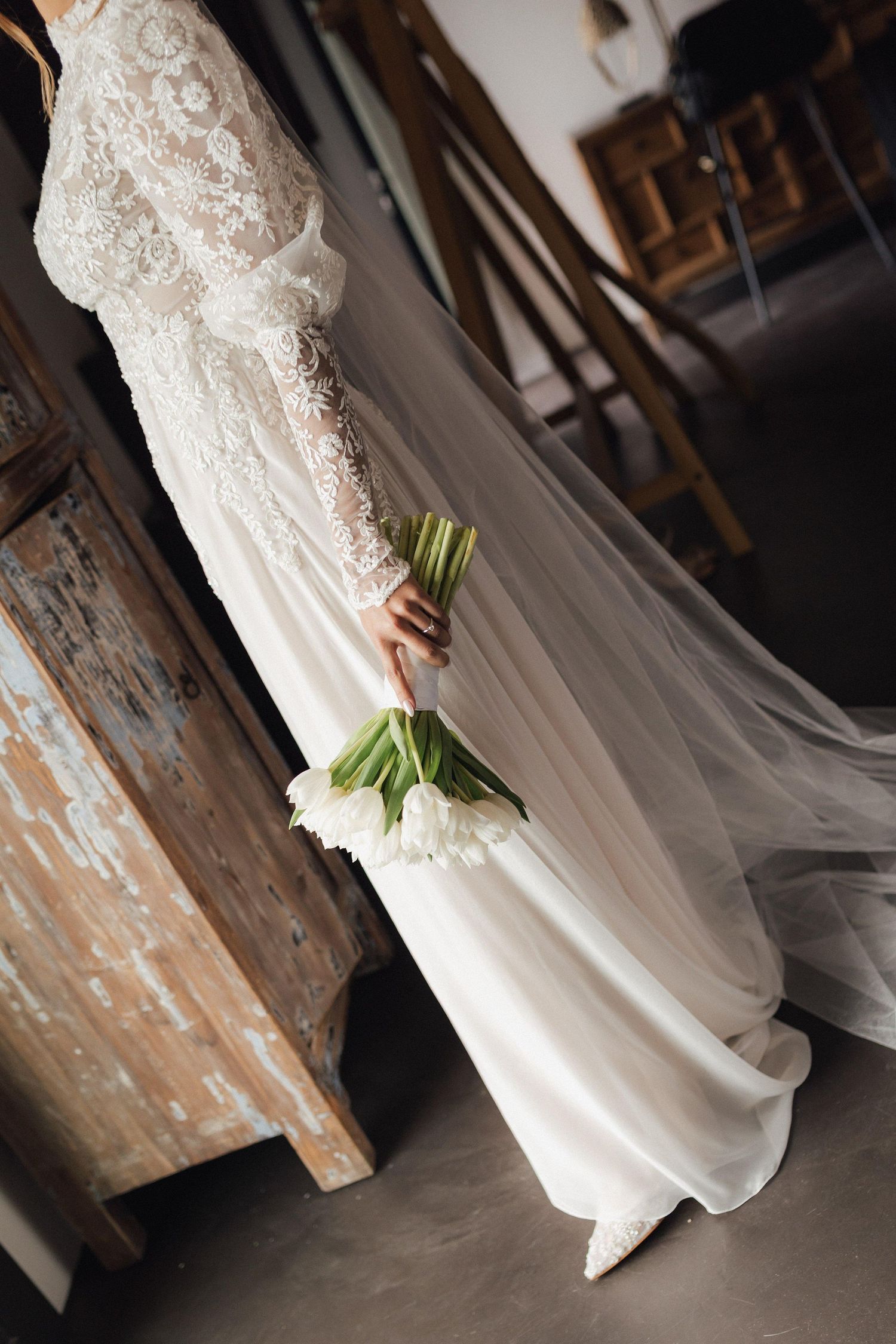 Elegant lace wedding dress with flowing fabric photographed against a rustic background.