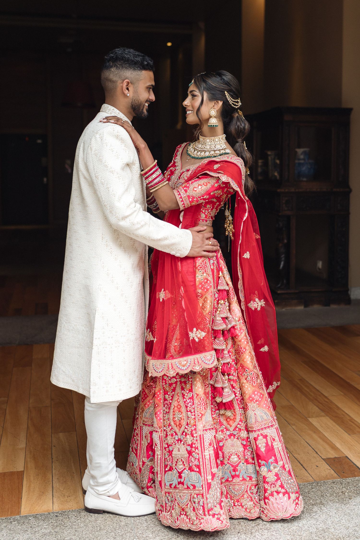 Traditional Indian wedding couple in red lehenga and white sherwani during their ceremony.