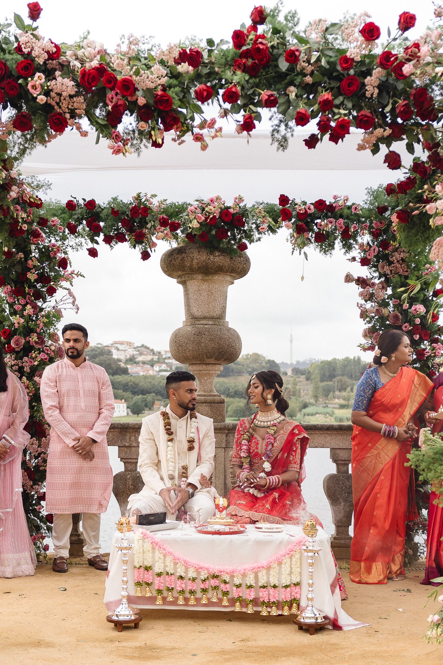 Traditional Indian wedding ceremony under a floral arch with red roses and white decor.